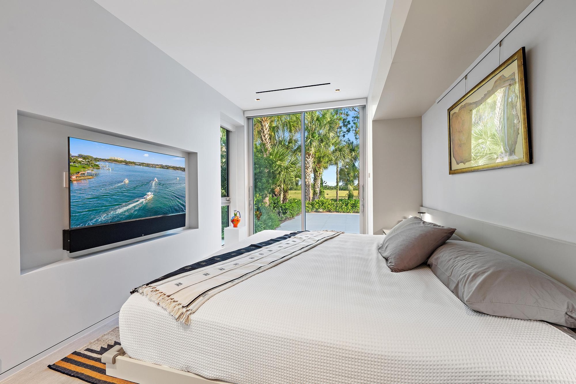 Recessed wall-mounted television with soundbar, full-height sliding glass doors, and a built-in headboard with integrated lighting