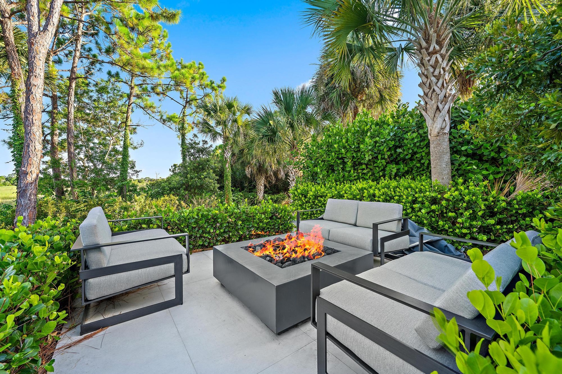 Paved patio with a built-in fire pit, surrounded by lush landscaping and mature trees
