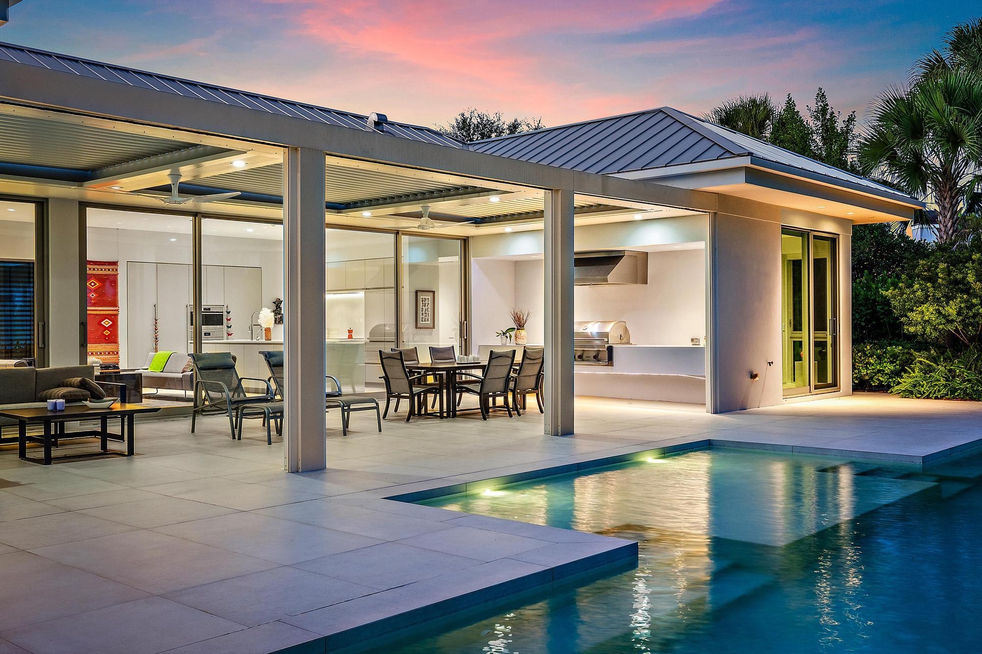 Modern residence featuring a resort-style backyard with an illuminated saltwater pool, expansive travertine-finish patio, and seamless indoor-outdoor 