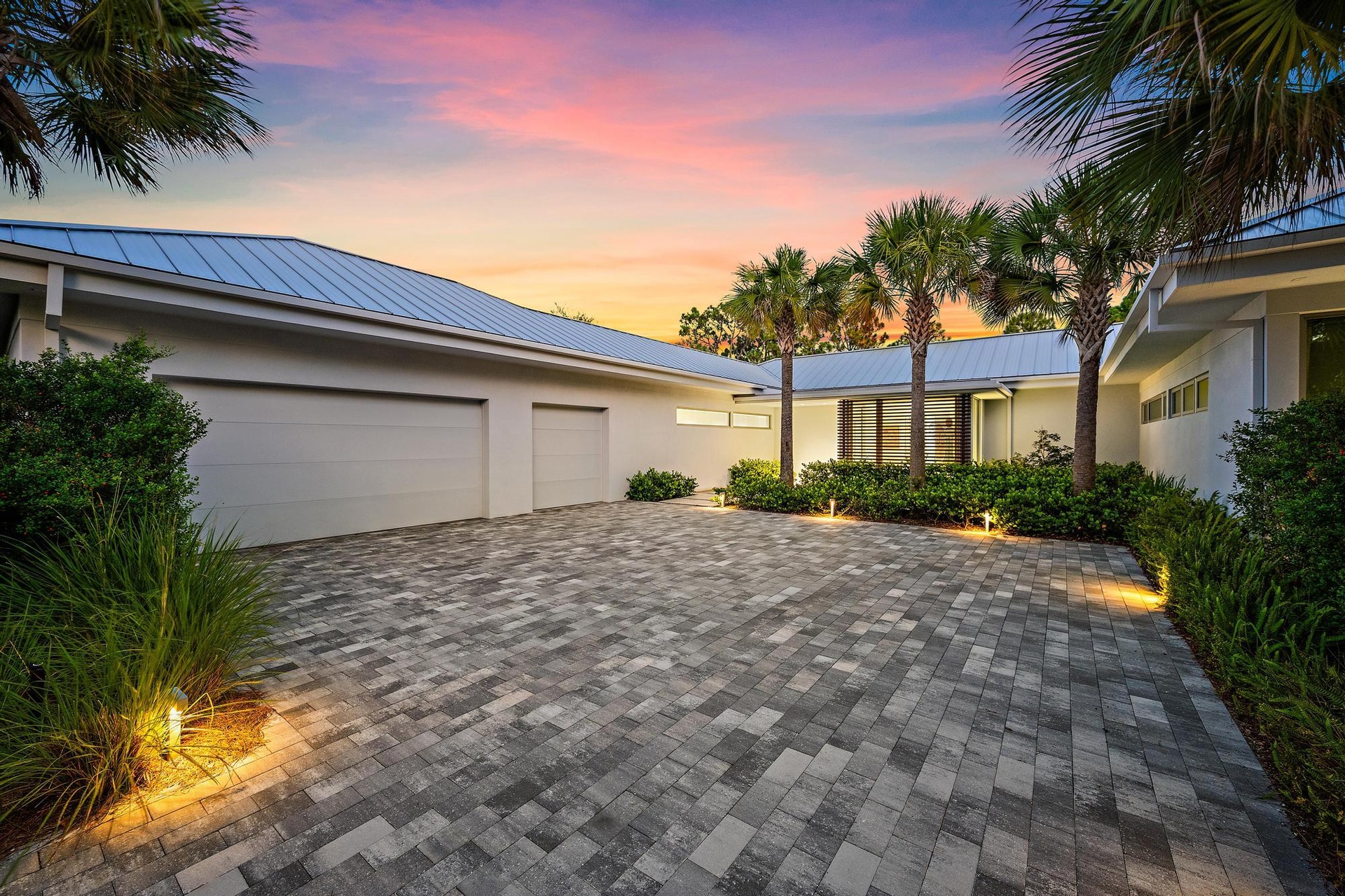 Modern exterior featuring a metal roof, two-car garage, and a paver driveway
