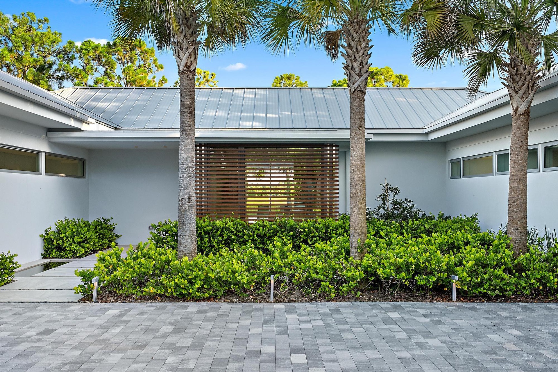 Modern residence featuring a clean-lined white exterior with standing-seam metal roofing, framed by three mature palm trees