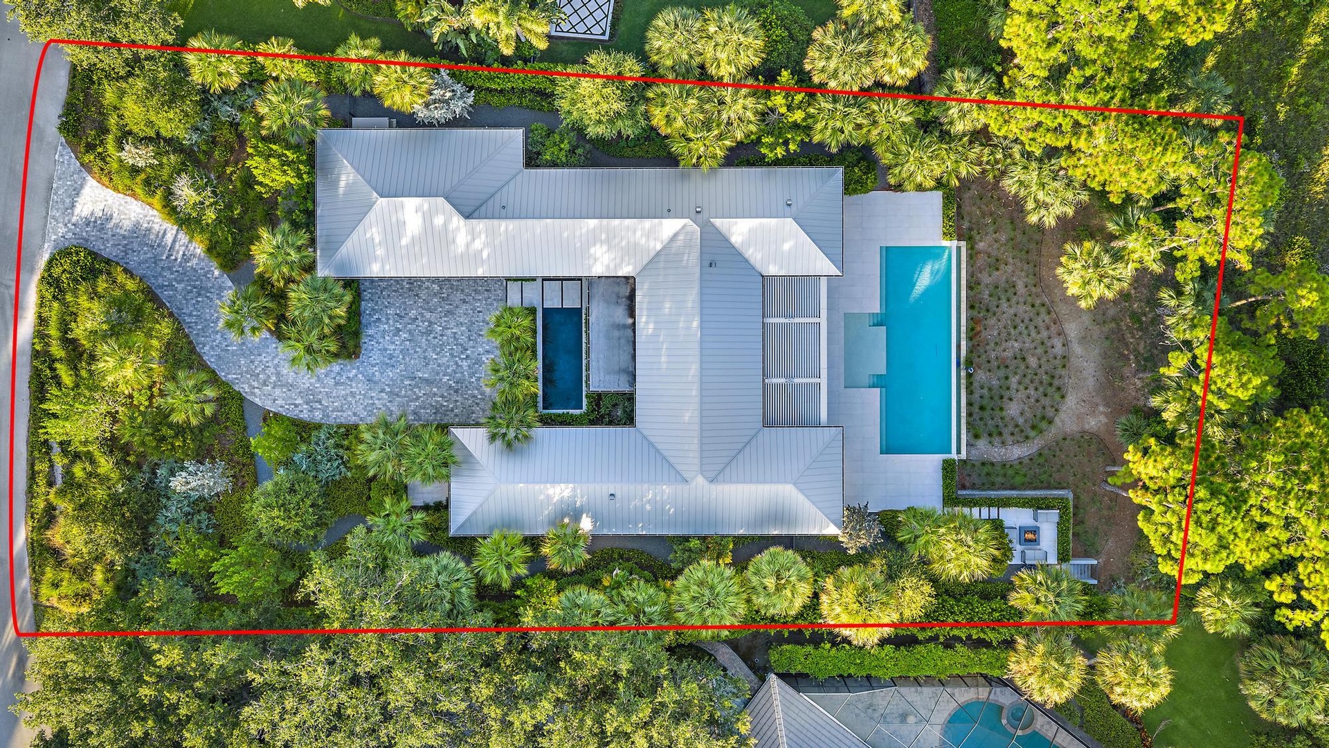 Expansive property featuring a winding paver driveway, lush landscaping, two distinct swimming pools, and a private outdoor lounge area