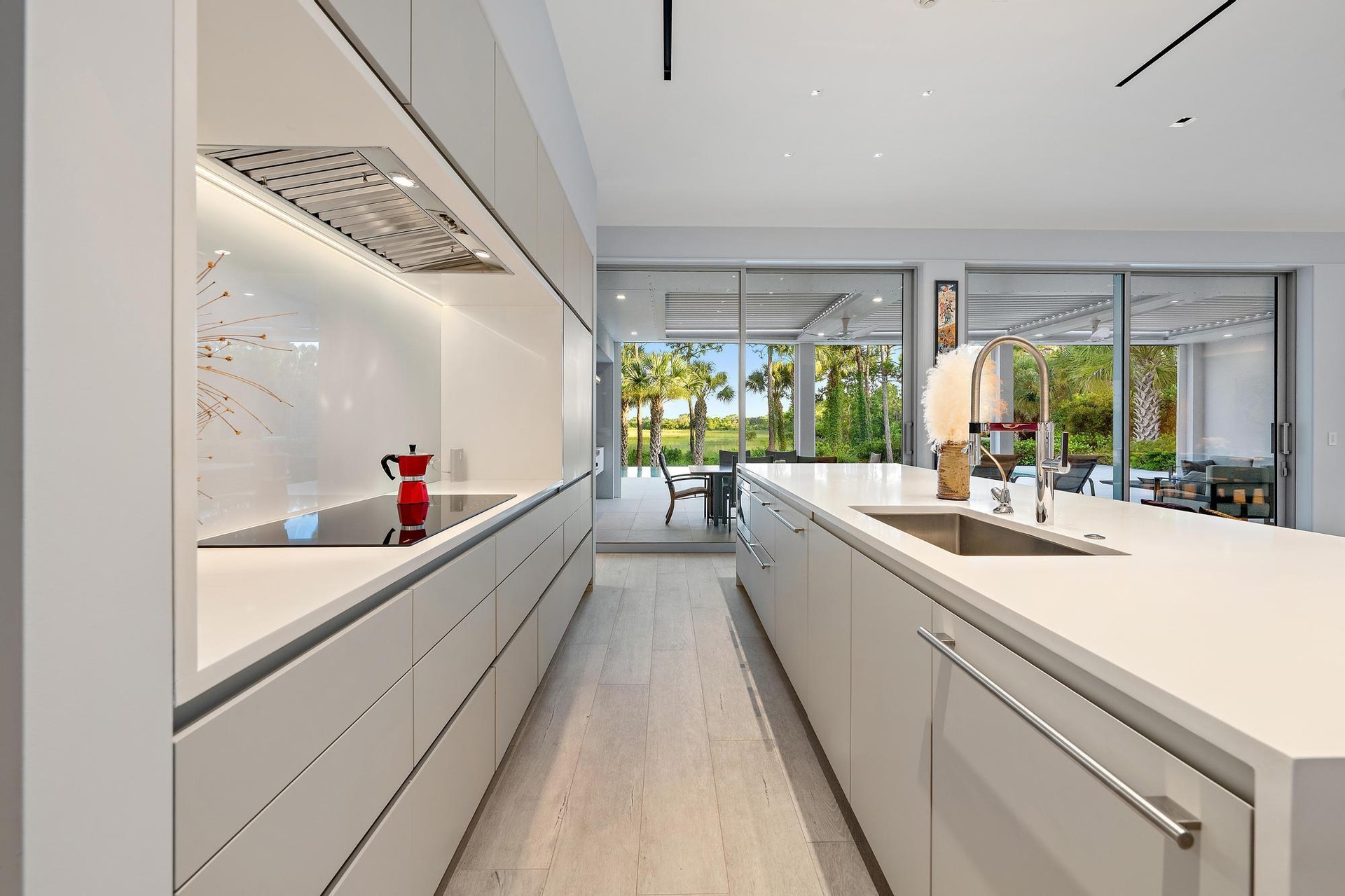 Modern kitchen featuring white flat-panel cabinetry, light wood-finish flooring, a stainless steel sink, and a cooktop with an integrated range hood