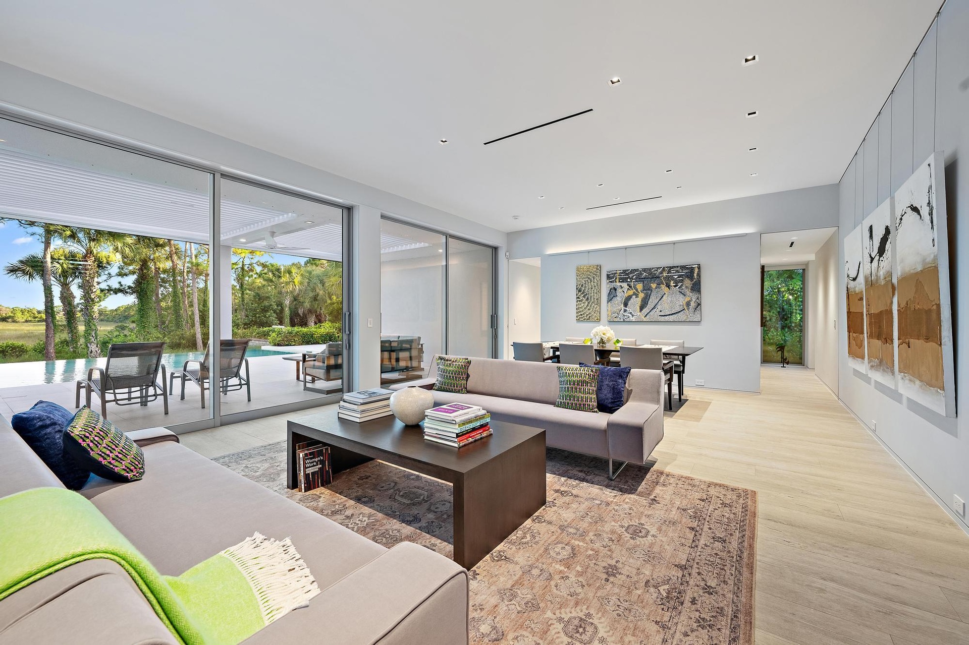 Sophisticated open-concept living space featuring floor-to-ceiling sliding glass doors opening to expansive outdoor grounds, light wood-finish floorin
