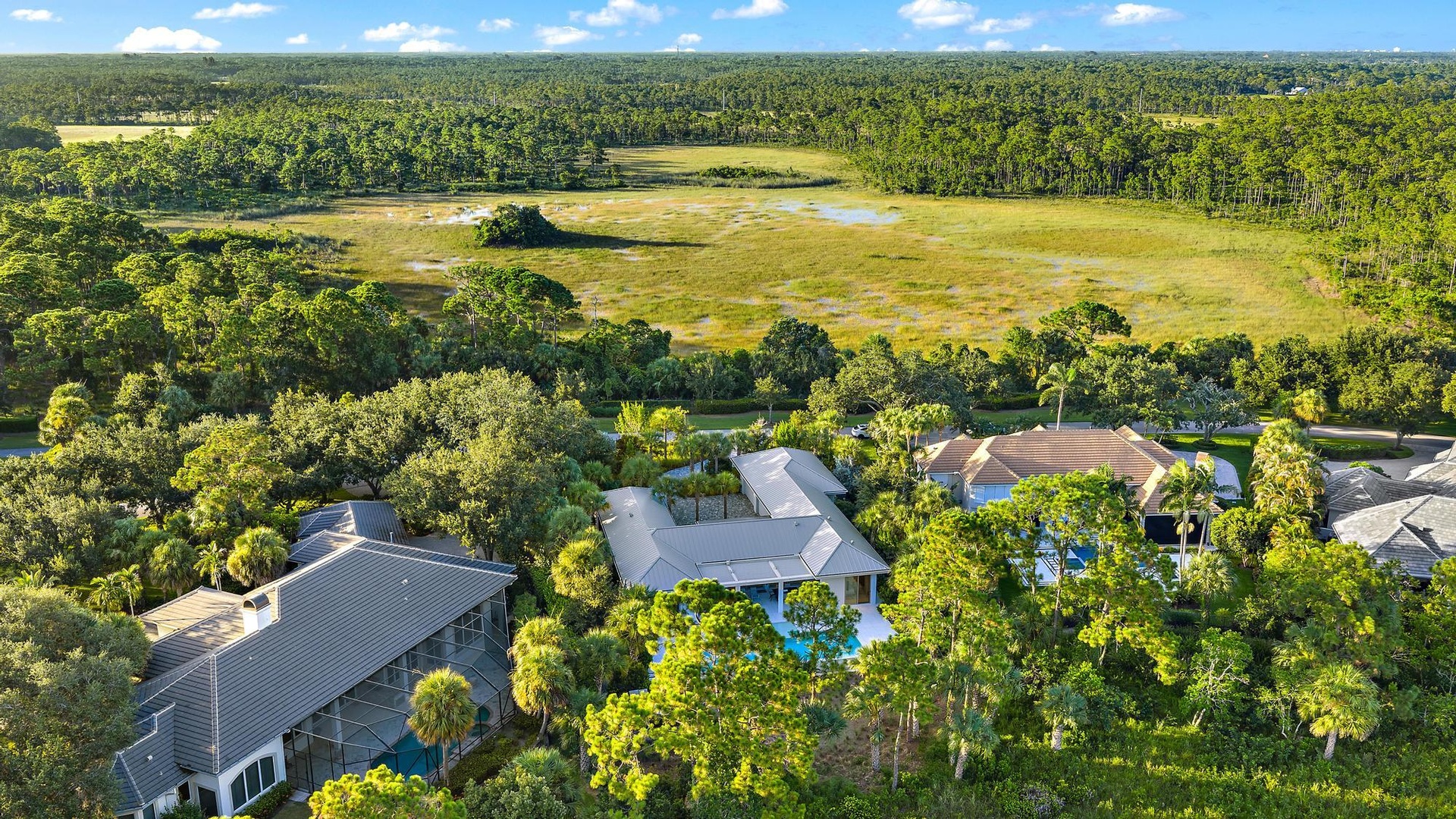 Aerial view of this expansive residential compound featuring a modern primary residence with geometric architecture, resort-style saltwater swimming p