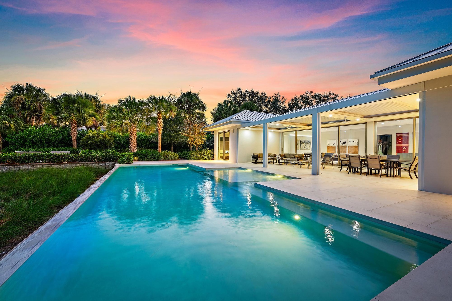 Expansive outdoor living area featuring a rectangular pool with integrated steps, a covered patio, a paver patio, and mature landscaping