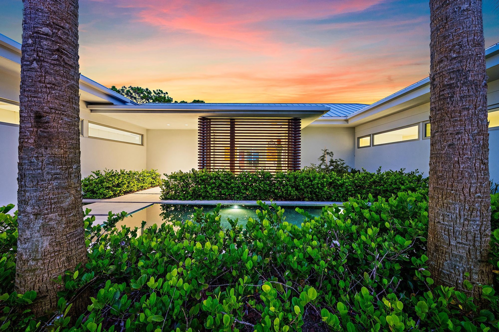 Modern exterior architecture with a flat roofline, horizontal slat detailing, and a reflective water feature