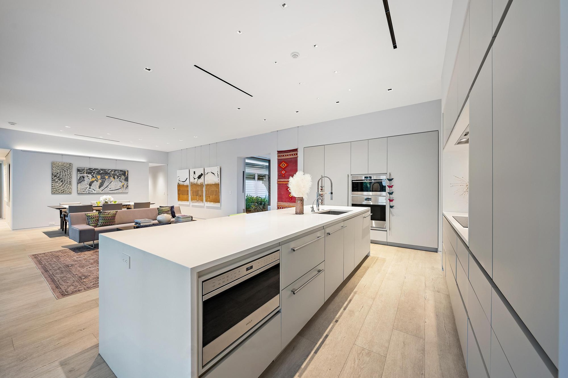 Open-concept kitchen with a large island featuring a built-in microwave, integrated appliances, and light wood-finish flooring