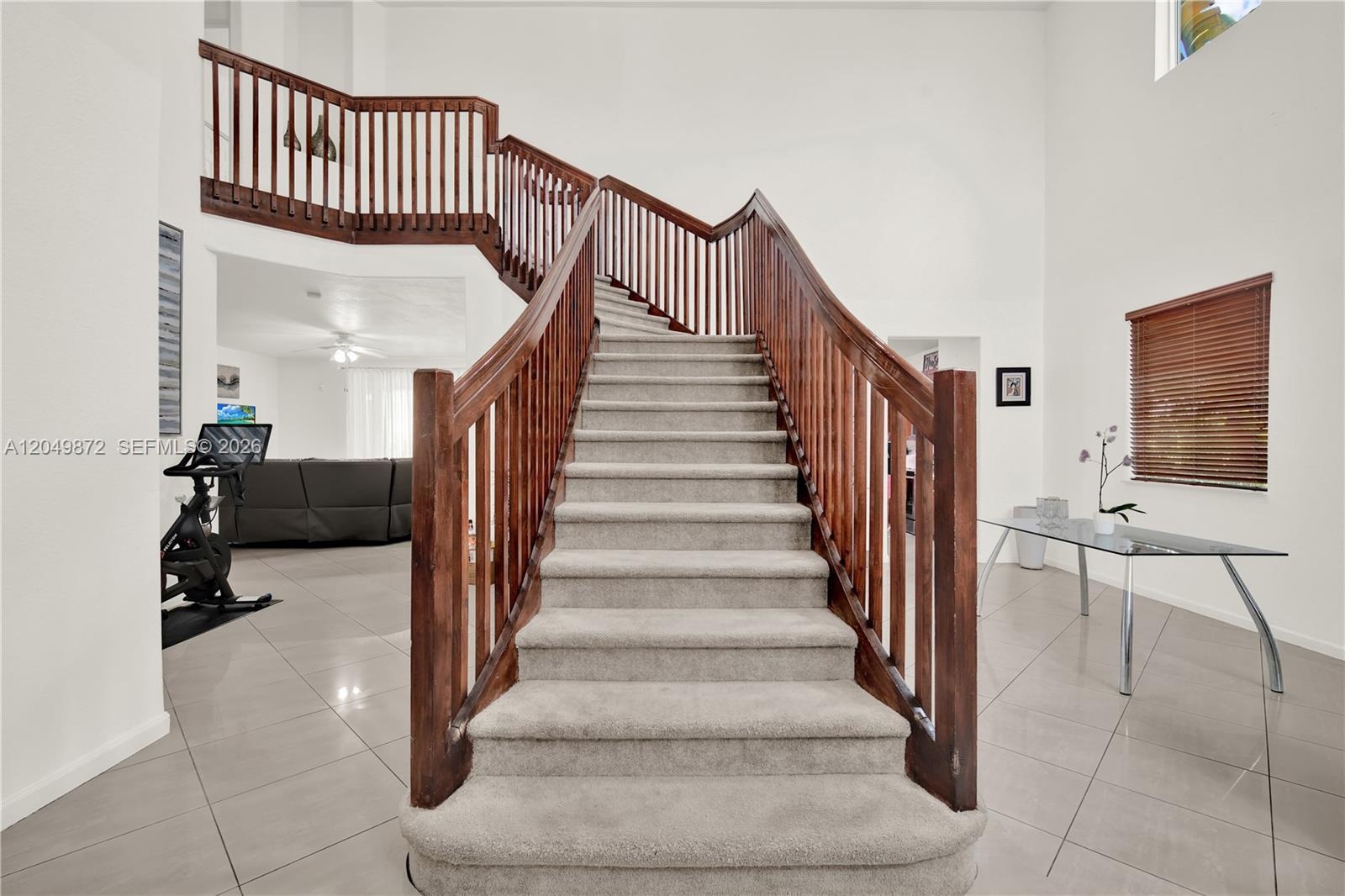 Two-story interior featuring high ceilings, neutral tile flooring, arched windows, and a wooden staircase railing