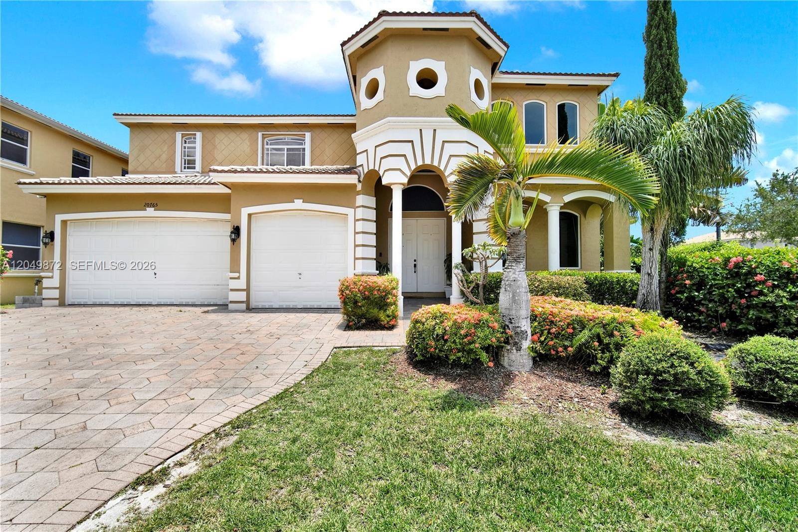 Two-story stucco exterior featuring a turreted entry, decorative arch detailing, two-car garage, and patterned paver driveway