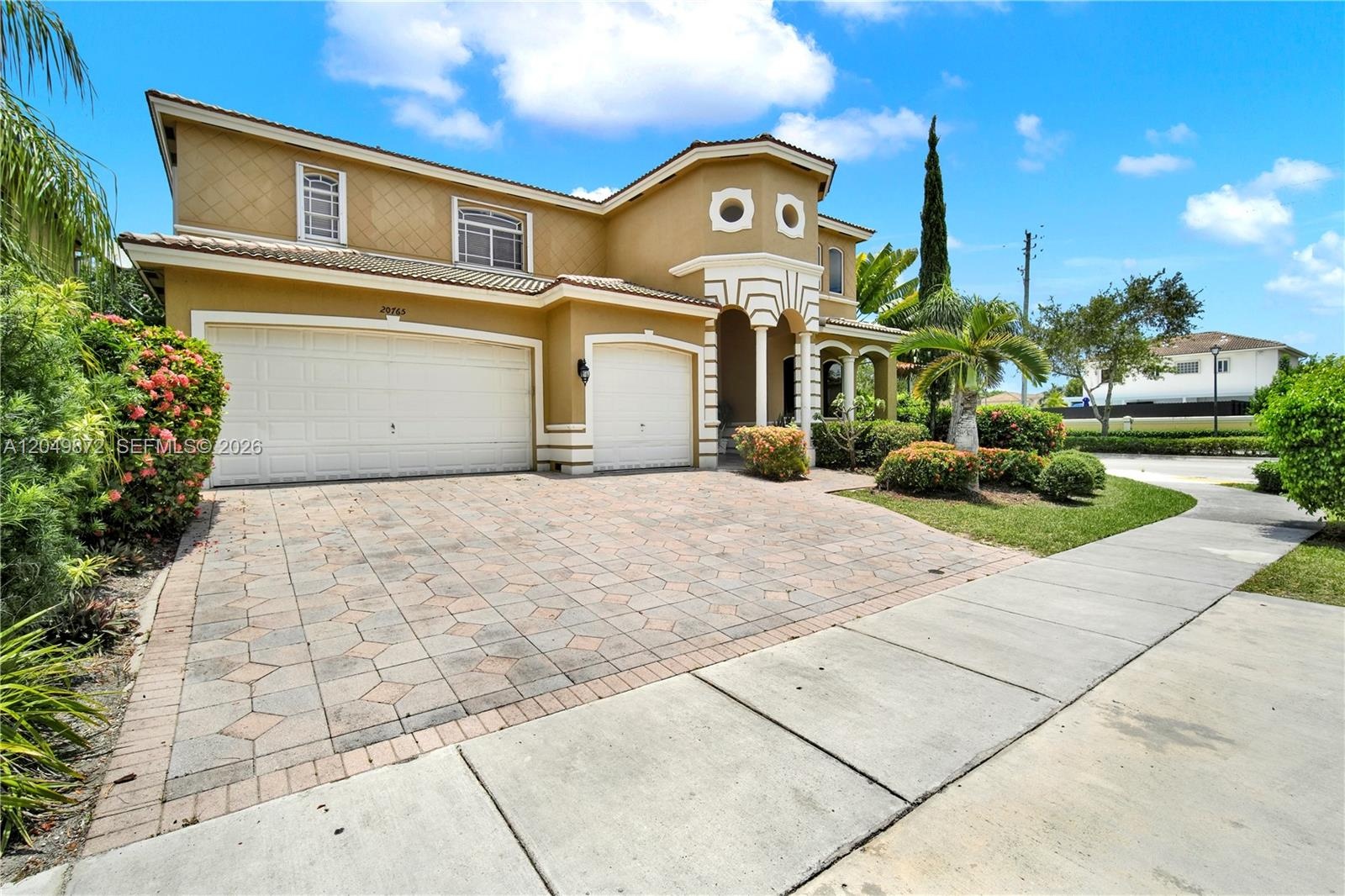 Two-story residence featuring a tile roof, brick-paver driveway, multi-car garage, turret-style entryway, and waterfront location