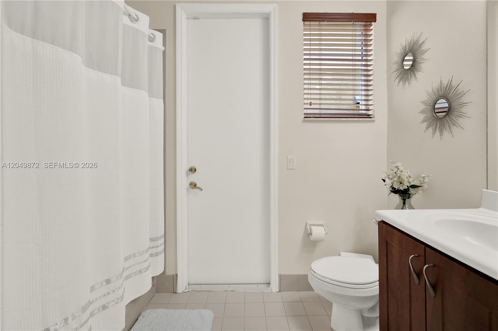 Neutral-toned tile flooring, large window with a deep sill, and dual-panel closet doors featuring white millwork, complete with a mounted ceiling fan 
