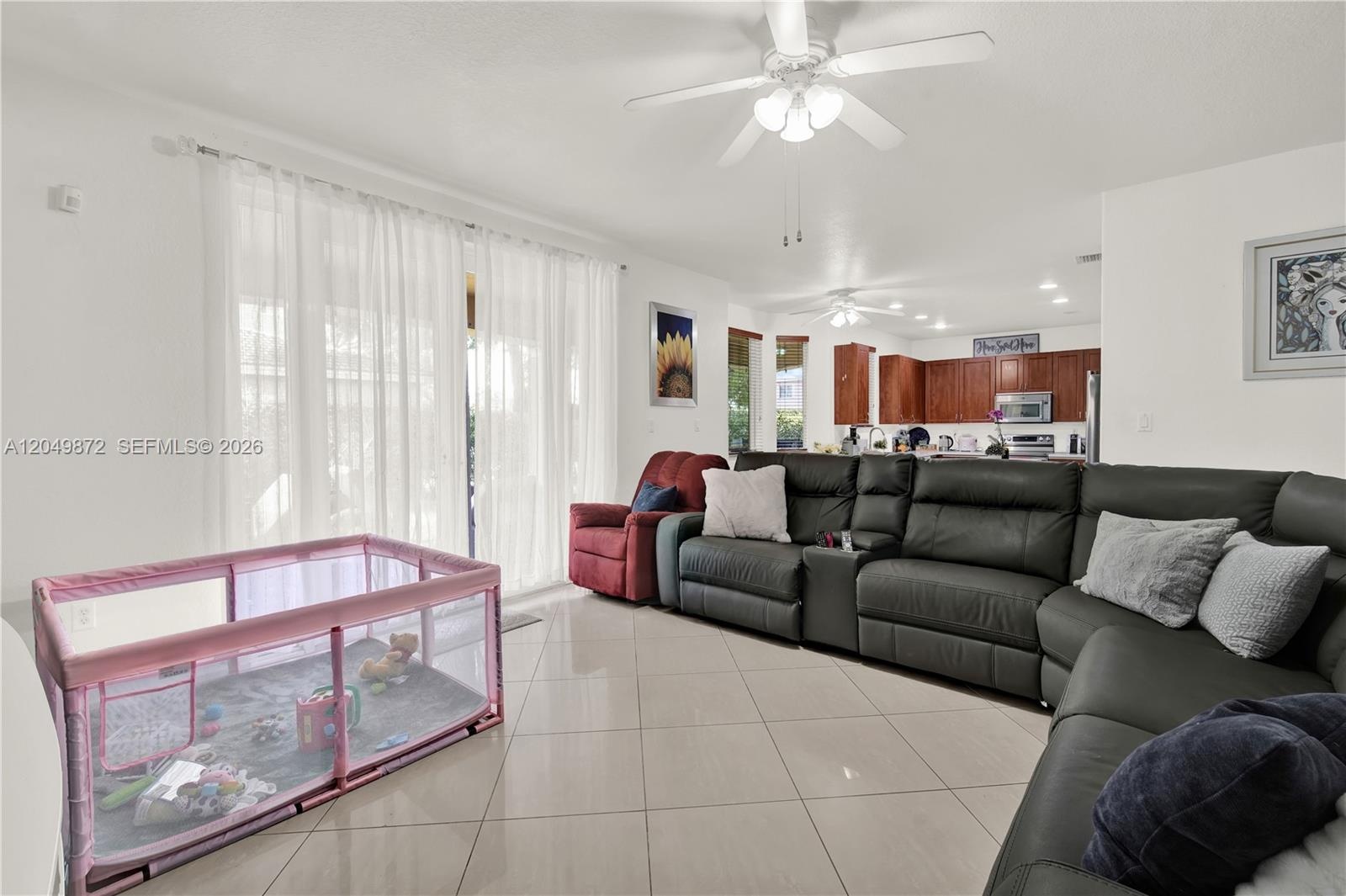 Large-format tile flooring, ceiling fan with integrated lighting, and full-height glass-paneled double doors providing outdoor access