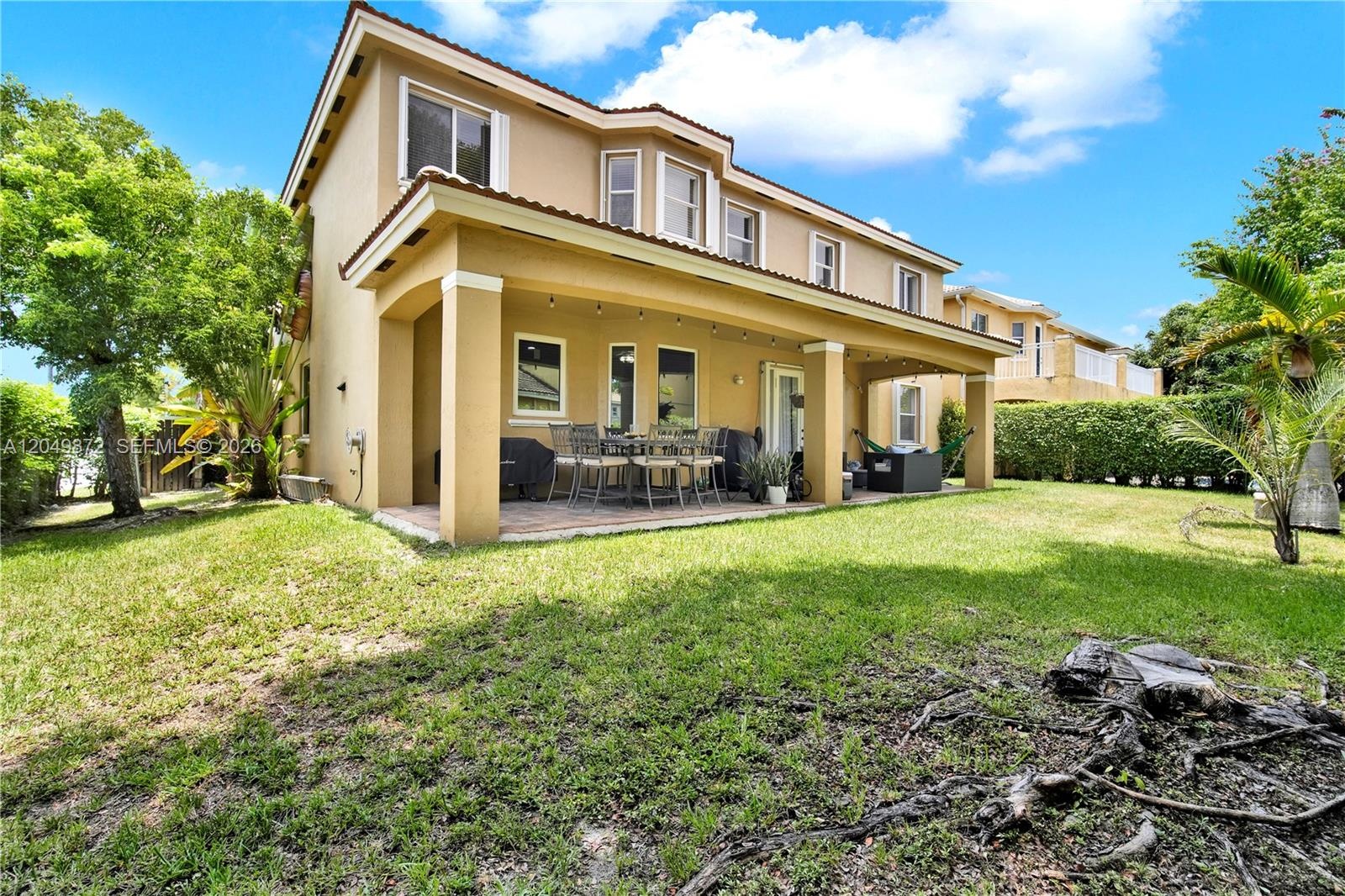 Two-story residence featuring a stucco exterior, a covered rear patio with concrete flooring, and an expansive lawn