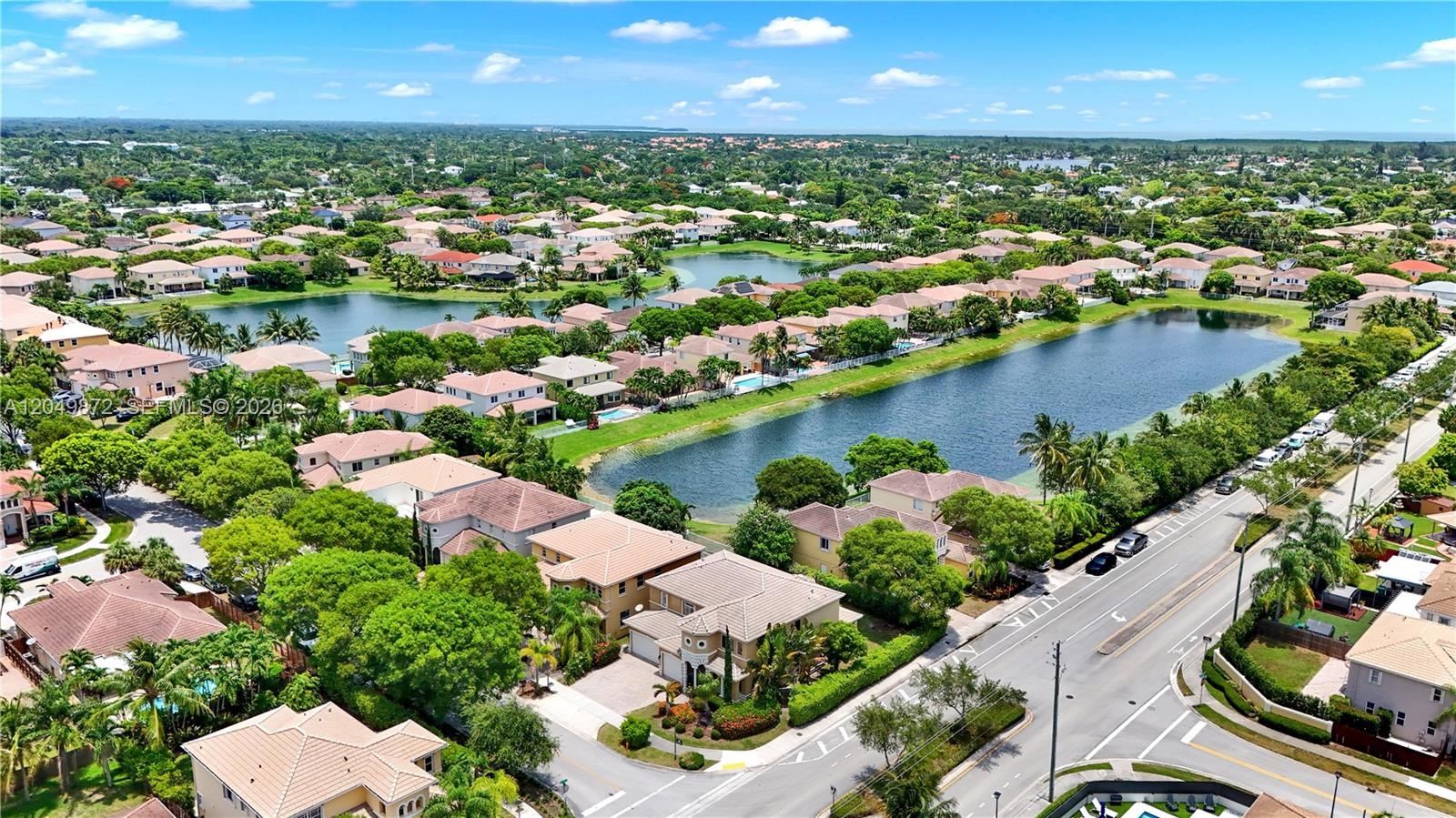 Aerial perspective featuring a two-story residence with a concrete tile roof, paved driveway, multi-car garage, and waterfront positioning