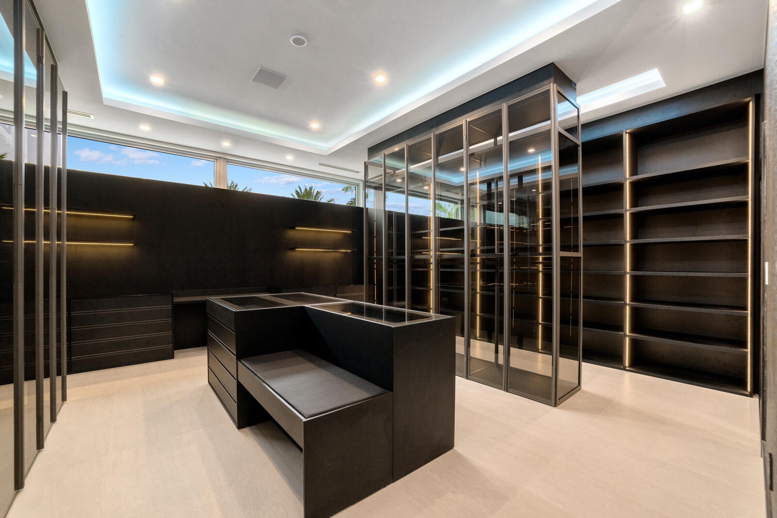 Extraordinary glass-enclosed boutique wardrobe with illuminated cabinetry, custom display cases, extensive storage, and a central dressing island with