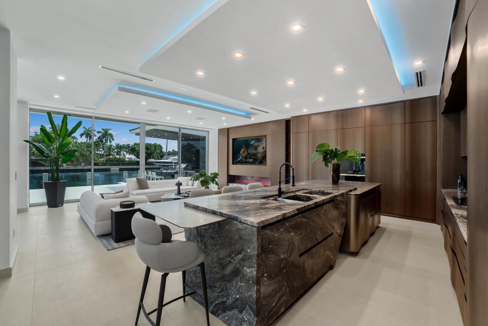 Open-concept kitchen and family room featuring a waterfall-edge natural-stone island, custom Italian cabinetry, architectural cove lighting, and unint