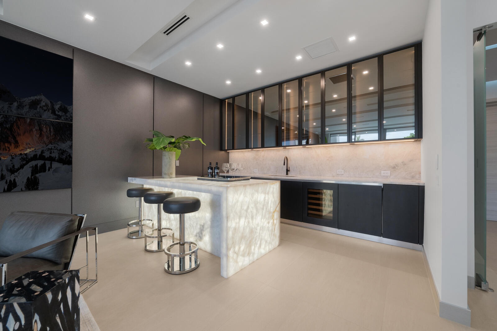 VIP suite’s full private bar showcasing a luminous waterfall-edge stone counter, seating for three, sink, wine refrigeration, illuminated backsplash, 