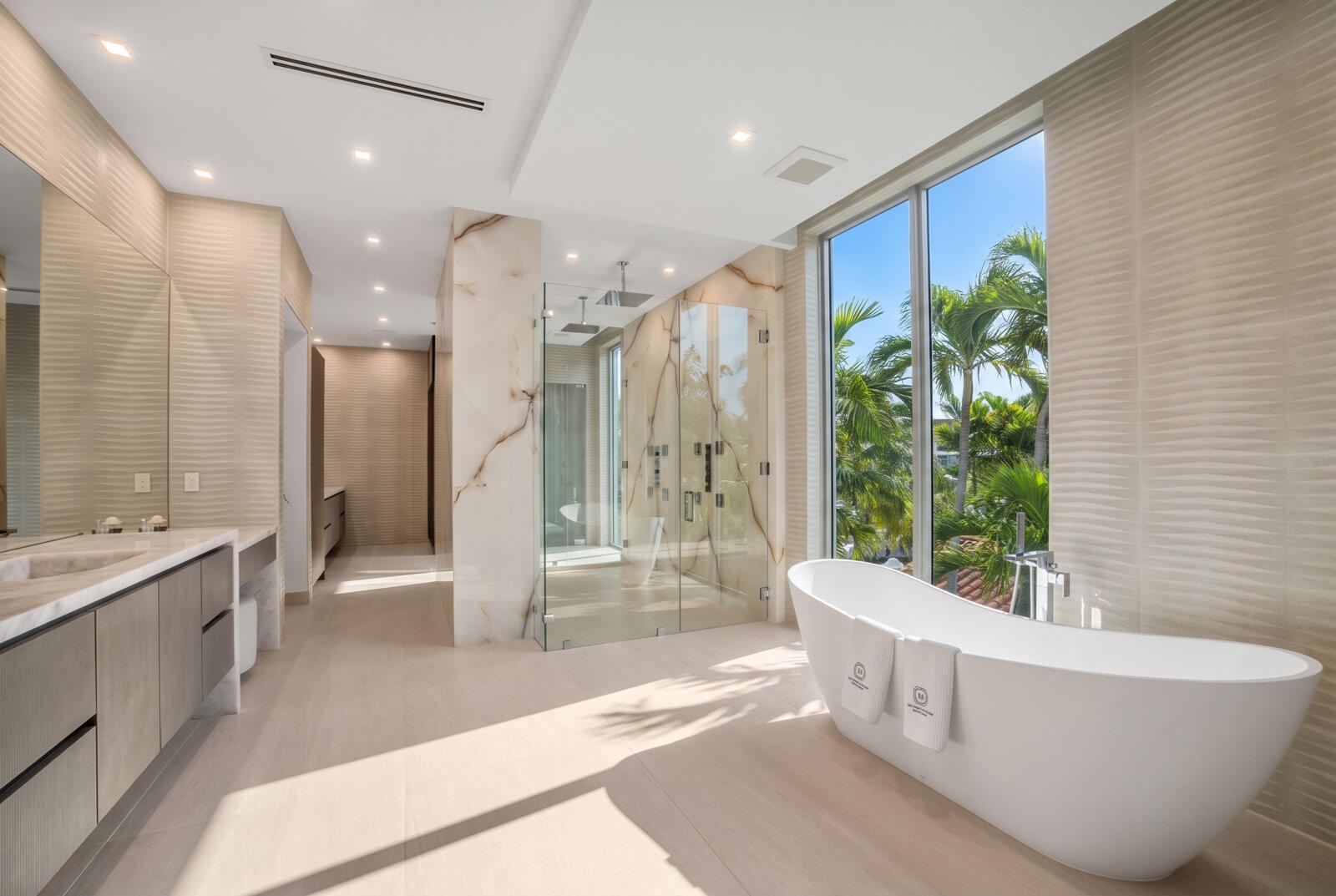 Spa-inspired primary bathroom with a sculptural freestanding tub, expansive windows, dual vanities, and an oversized glass shower wrapped in book-matc