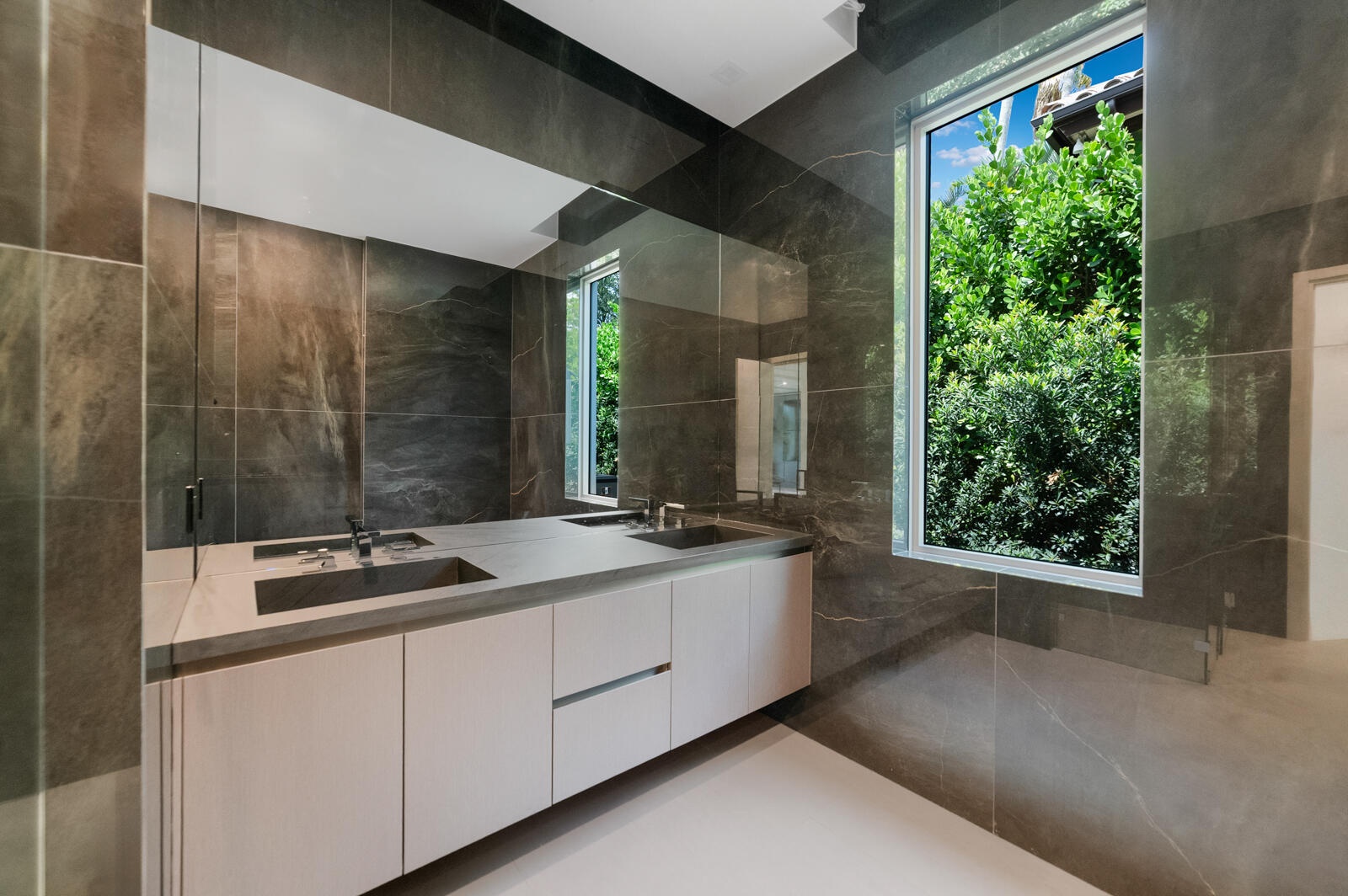 Luxurious en-suite bath finished with floor-to-ceiling stone, a floating dual-sink vanity, an oversized mirror, frameless glass shower, and abundant n
