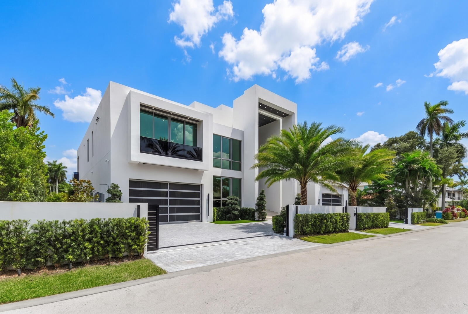 Left-side exterior view showcasing the home’s bold modern architecture, expansive floor-to-ceiling glass, sleek garage, gated motor court, and lush tr