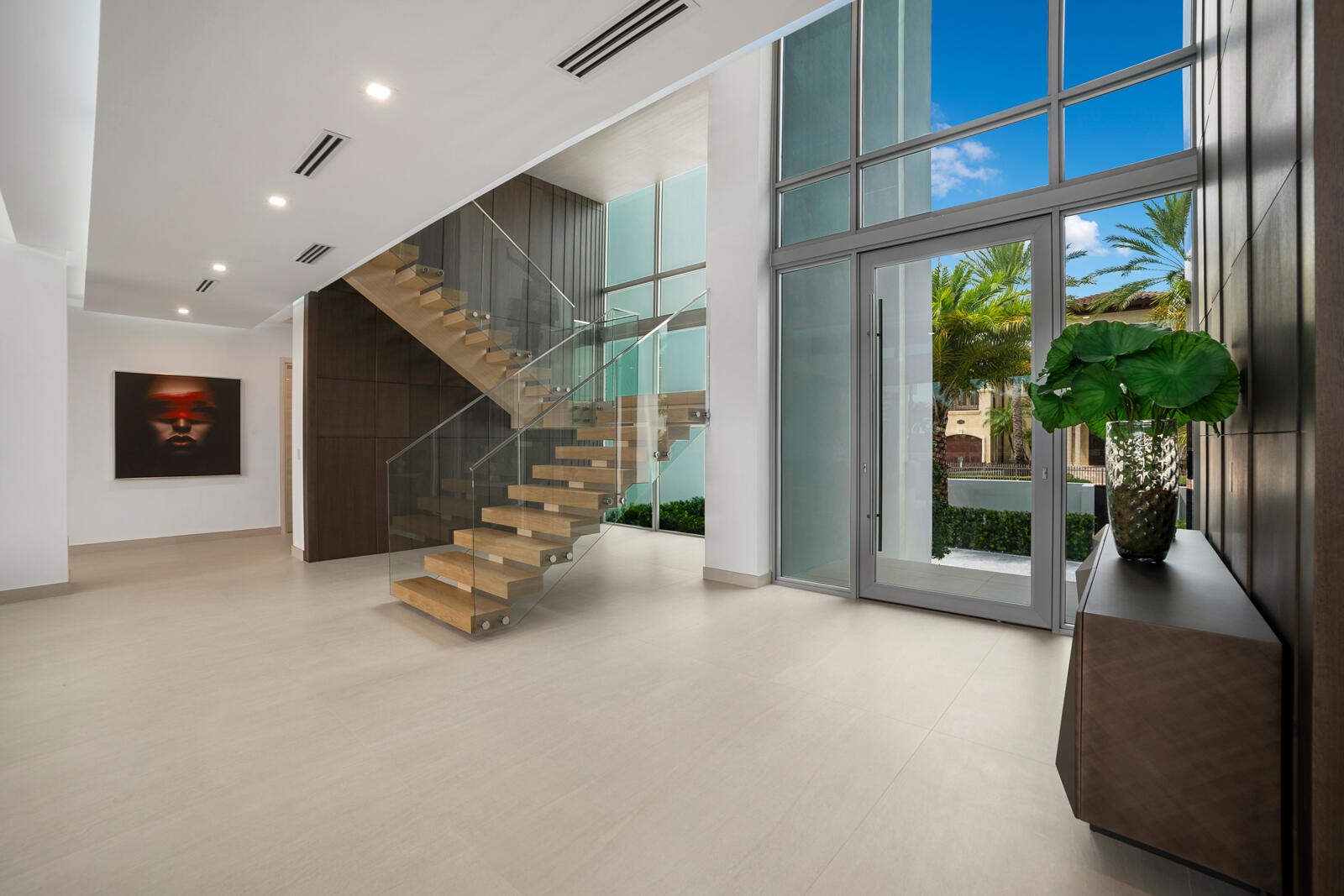 Dramatic first-floor entry showcasing soaring ceilings, a striking wood-paneled feature wall, and a floating staircase with glass railings.
