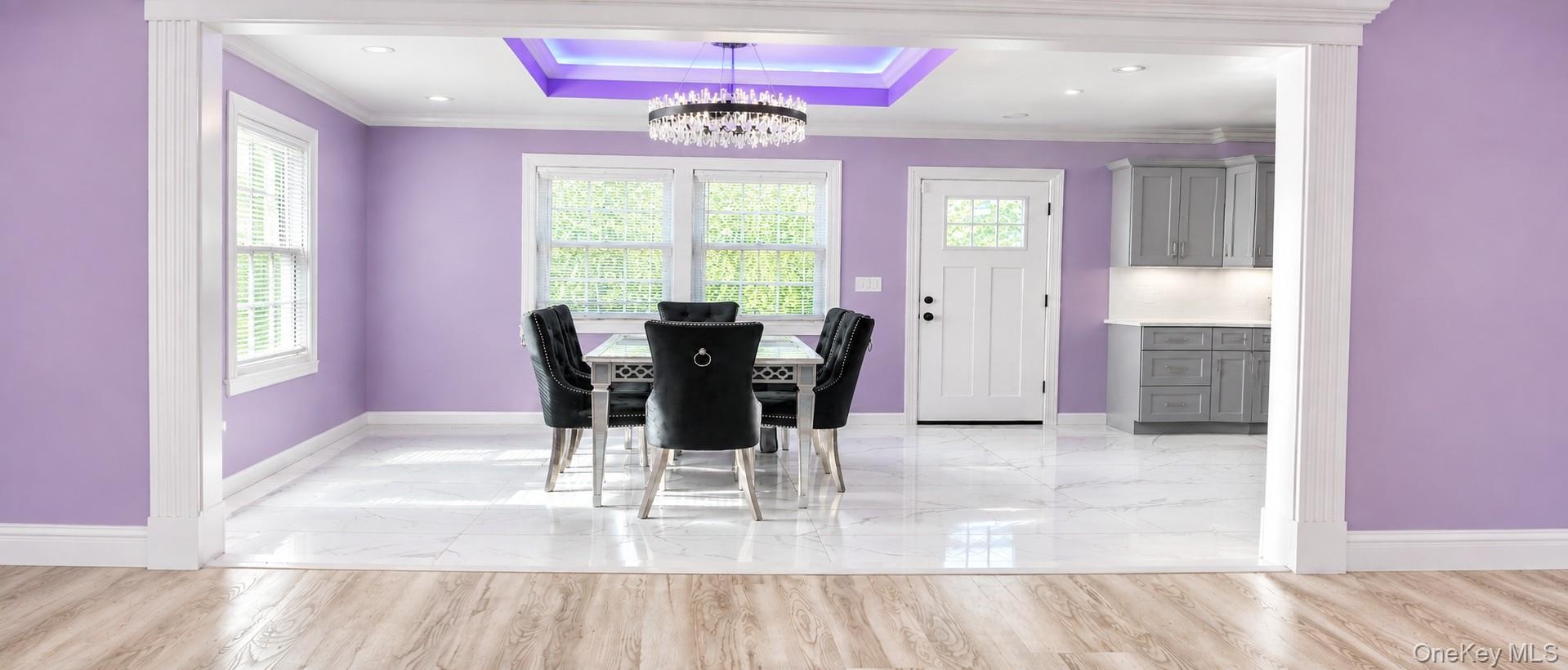 Recessed ceiling with accent lighting, crystal chandelier, white trim, and large windows