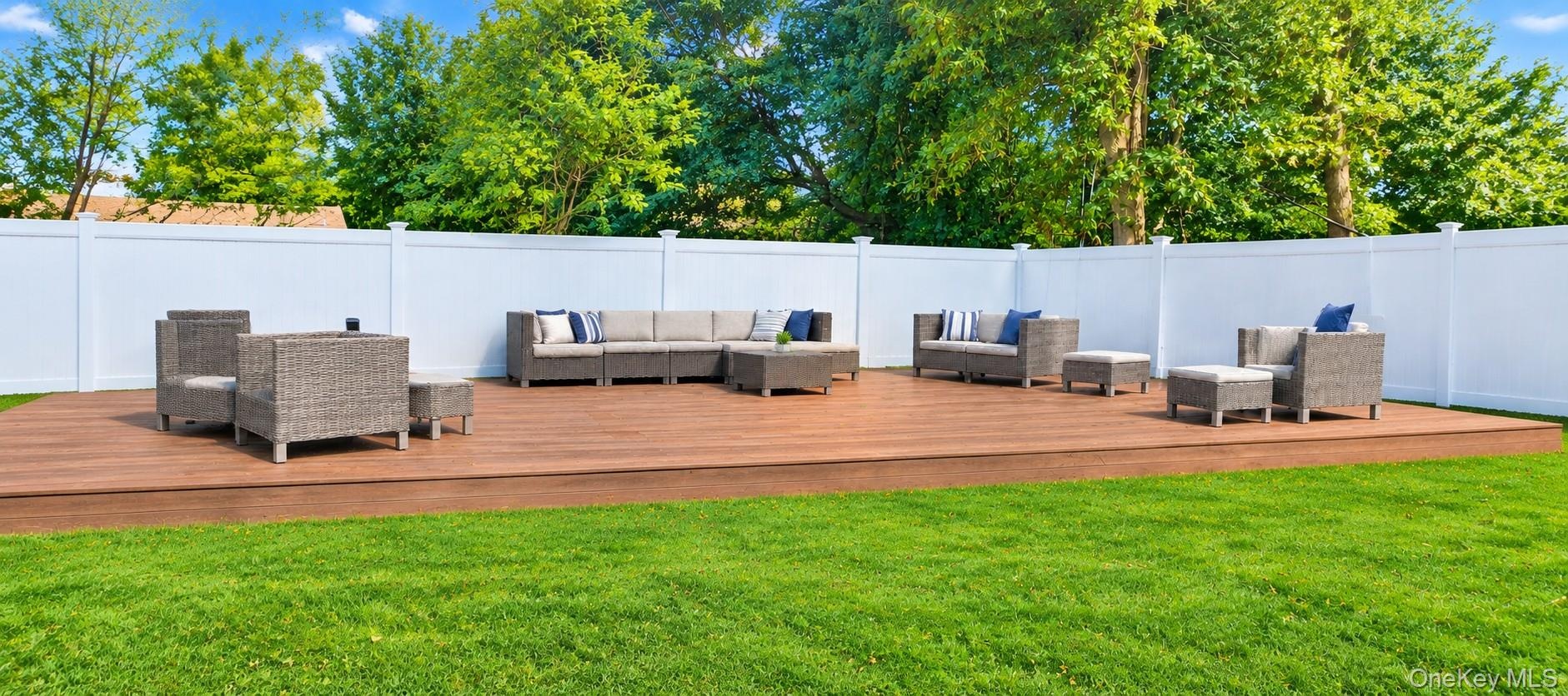 Expansive deck with a surrounding white privacy fence, featuring a lush green lawn and trees.