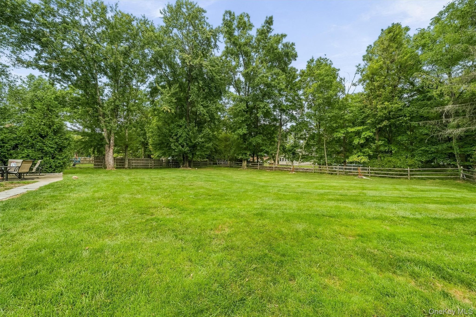Expansive green lawn framed by mature trees and a rustic wooden fence