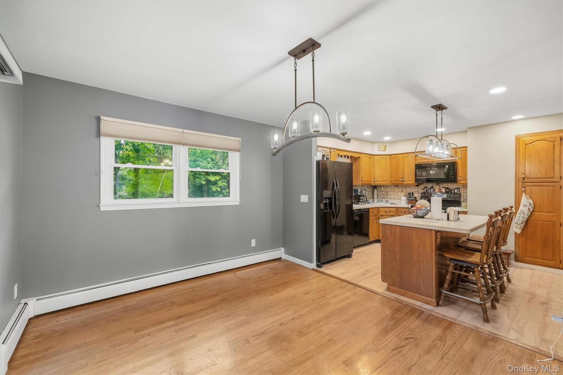 Hardwood flooring, kitchen island with counter seating, wood cabinetry, built-in microwave, and pendant lighting fixtures