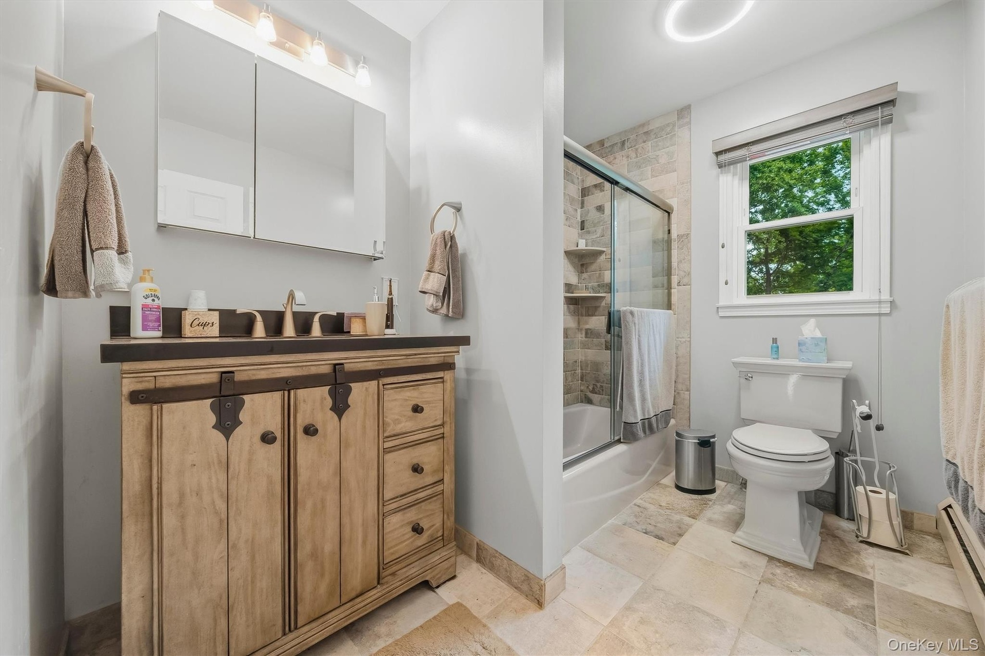 Wood-finish vanity with dark countertop, dual mirrored medicine cabinet, and a glass-enclosed shower with tiled surround