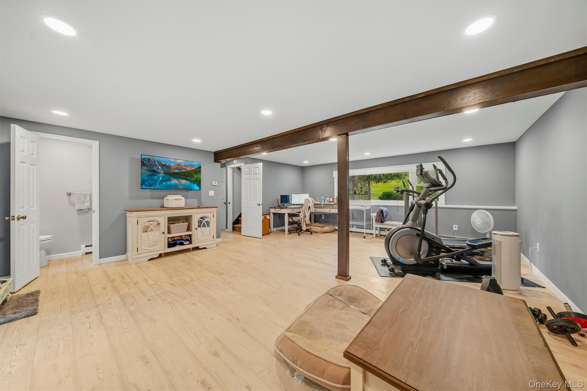 Recessed ceiling lighting, wood-finish flooring, exposed wood beam, large windows, and a separate room with a toilet and towel bar