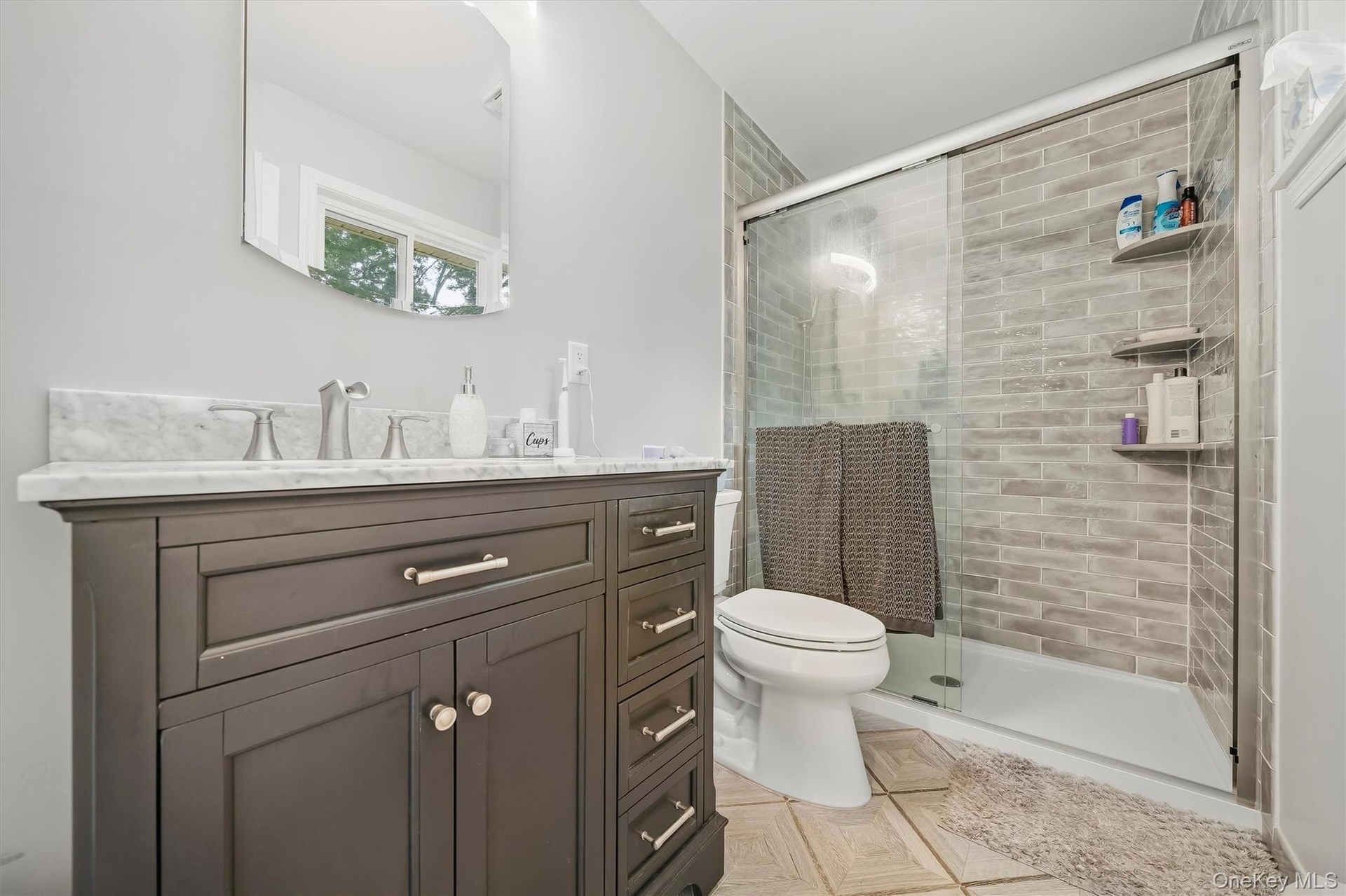 Dark wood vanity with a white marble countertop, brushed nickel faucet, and an arched frameless mirror