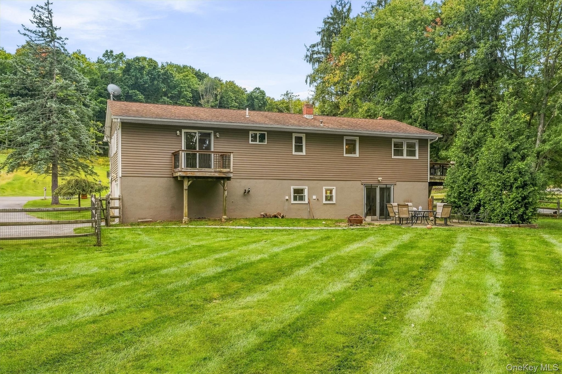 Expansive green space featuring a wood fence, mature trees, and a ground-level patio