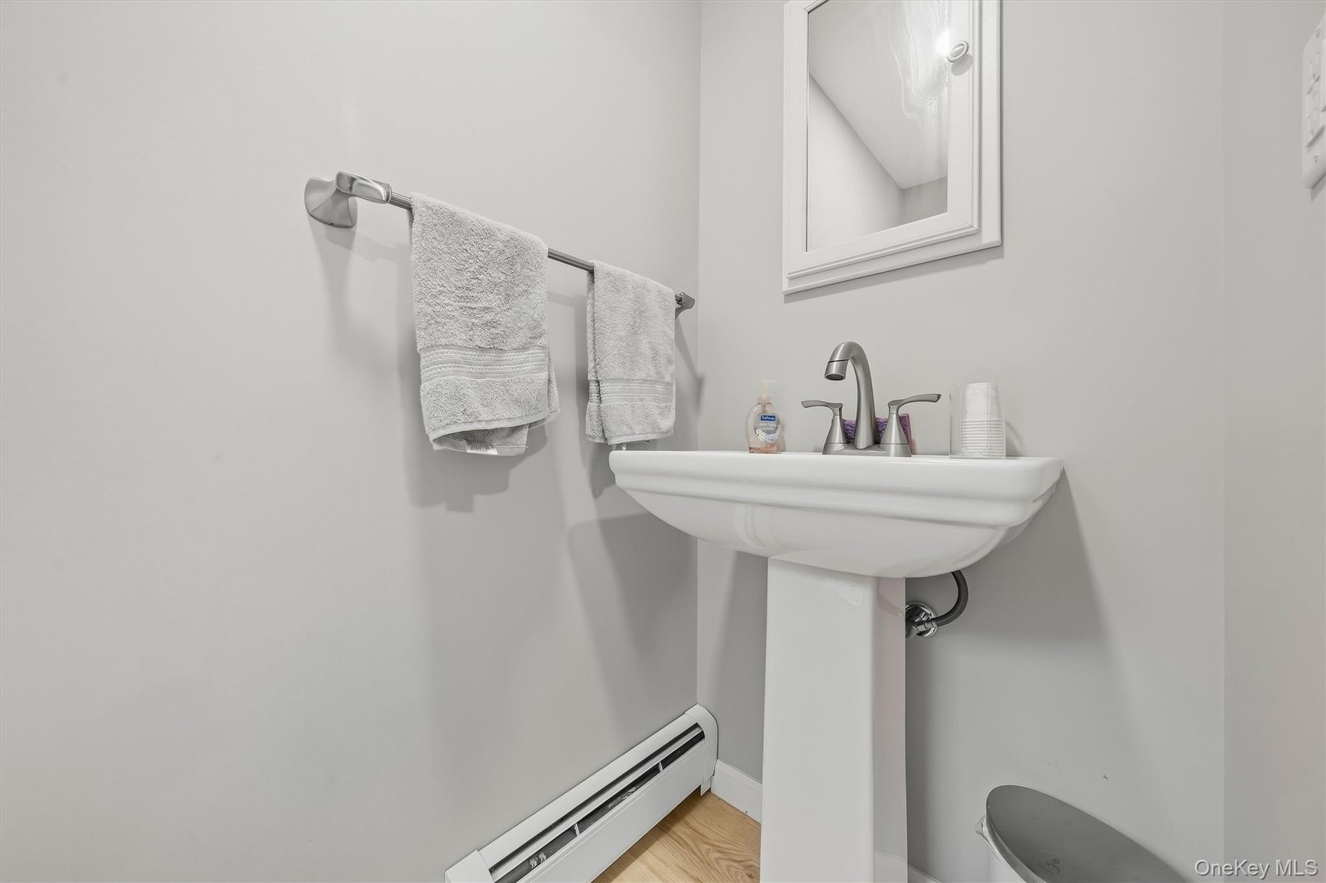 Pedestal sink with a polished chrome faucet, mirrored medicine cabinet, and light-toned wood-finish flooring
