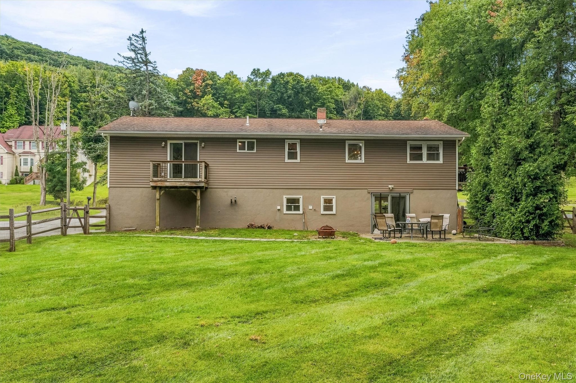Expansive green lawn with a split-rail fence, rear balcony, and lower-level patio area