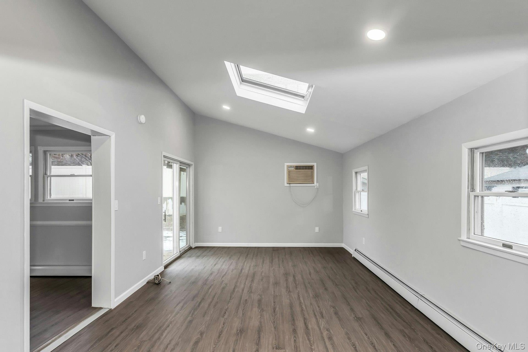 Vaulted ceiling with an integrated skylight, wood-finish flooring, recessed lighting, white baseboards, and sliding glass doors