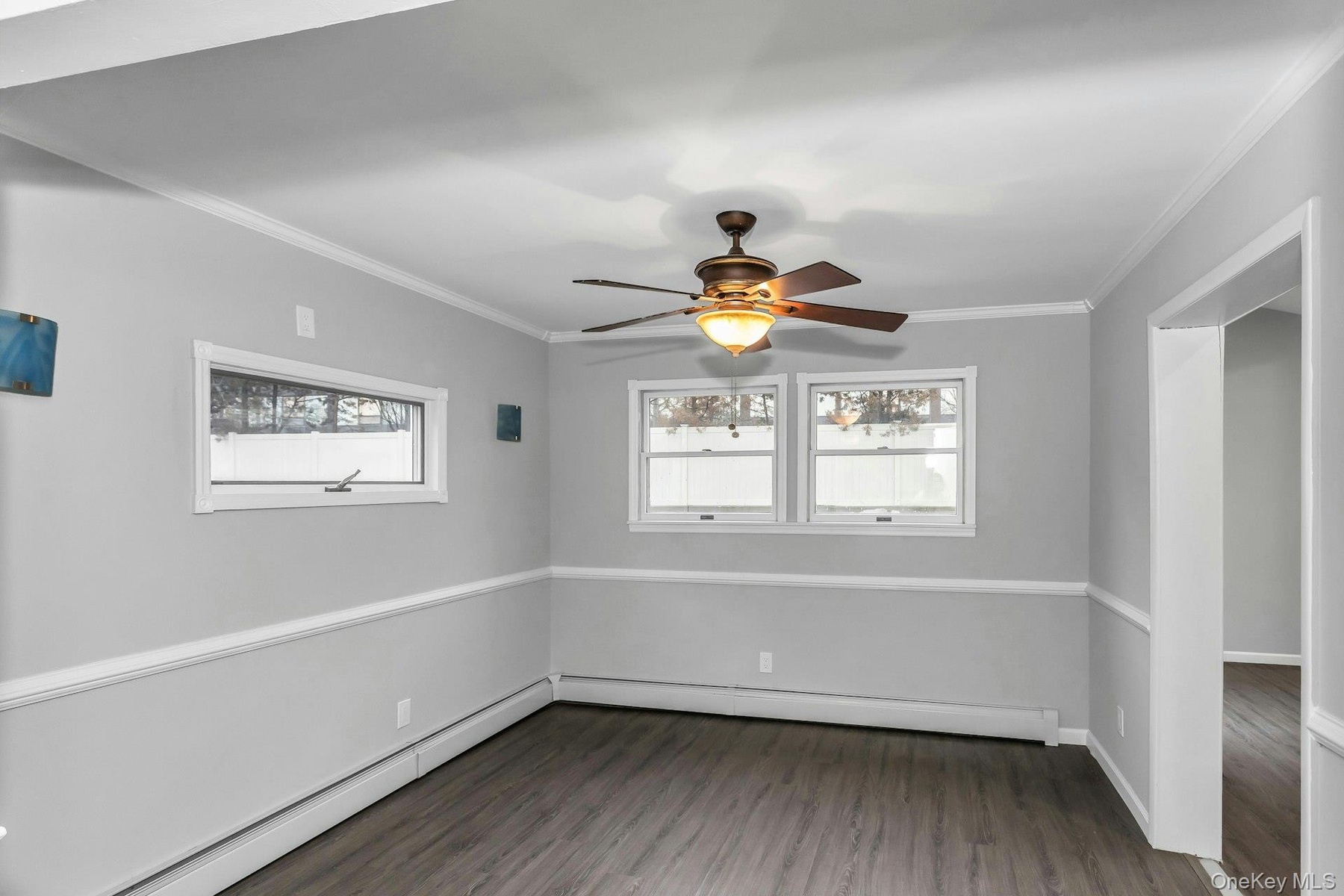 Spacious room featuring wood-finish flooring, light gray walls with white chair rail molding, and a bronze ceiling fan with integrated lighting