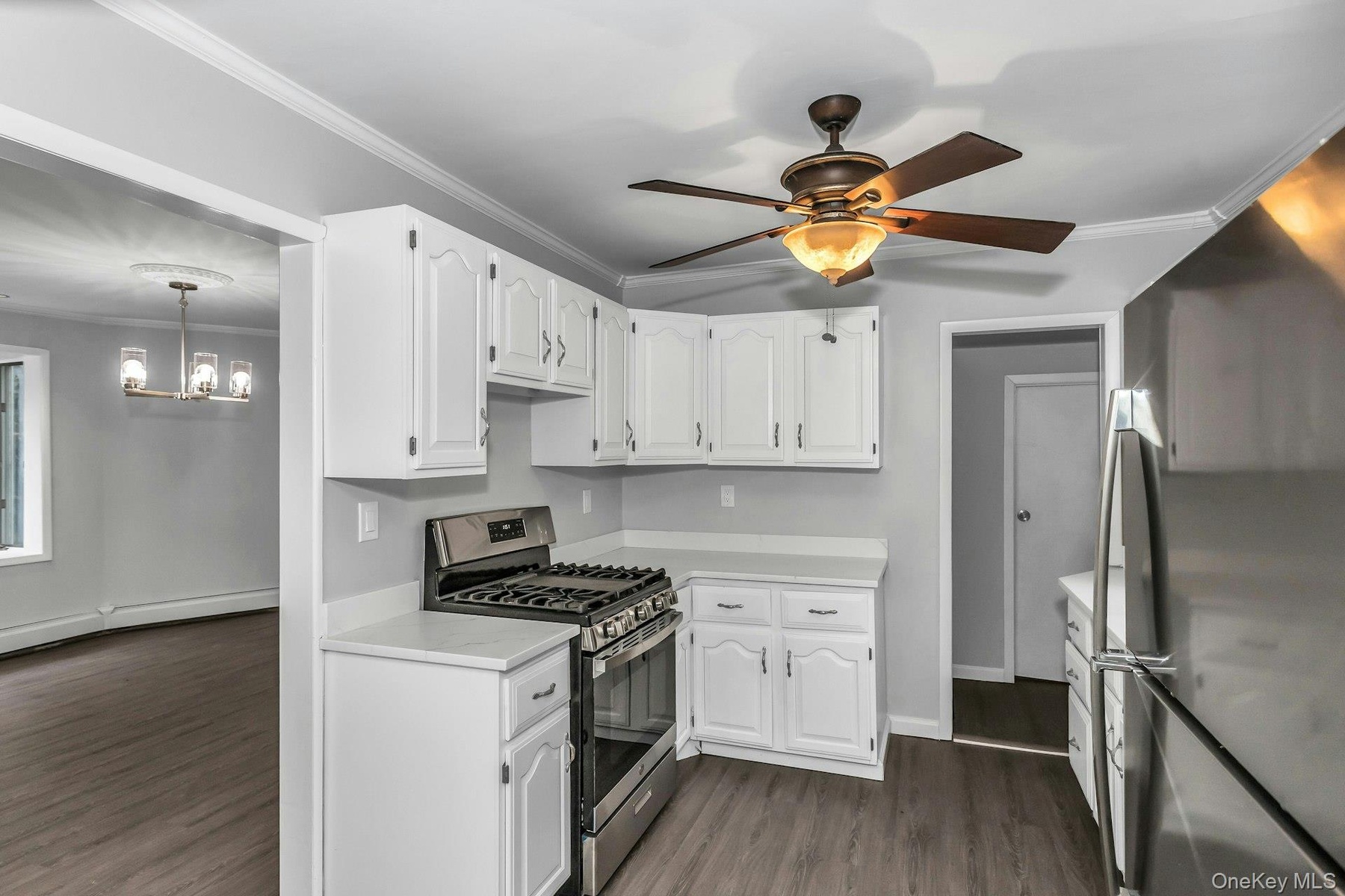 Eat-in kitchen featuring white cabinetry, light-toned countertops, stainless steel appliances, wood-finish flooring, and a ceiling fan with integrated