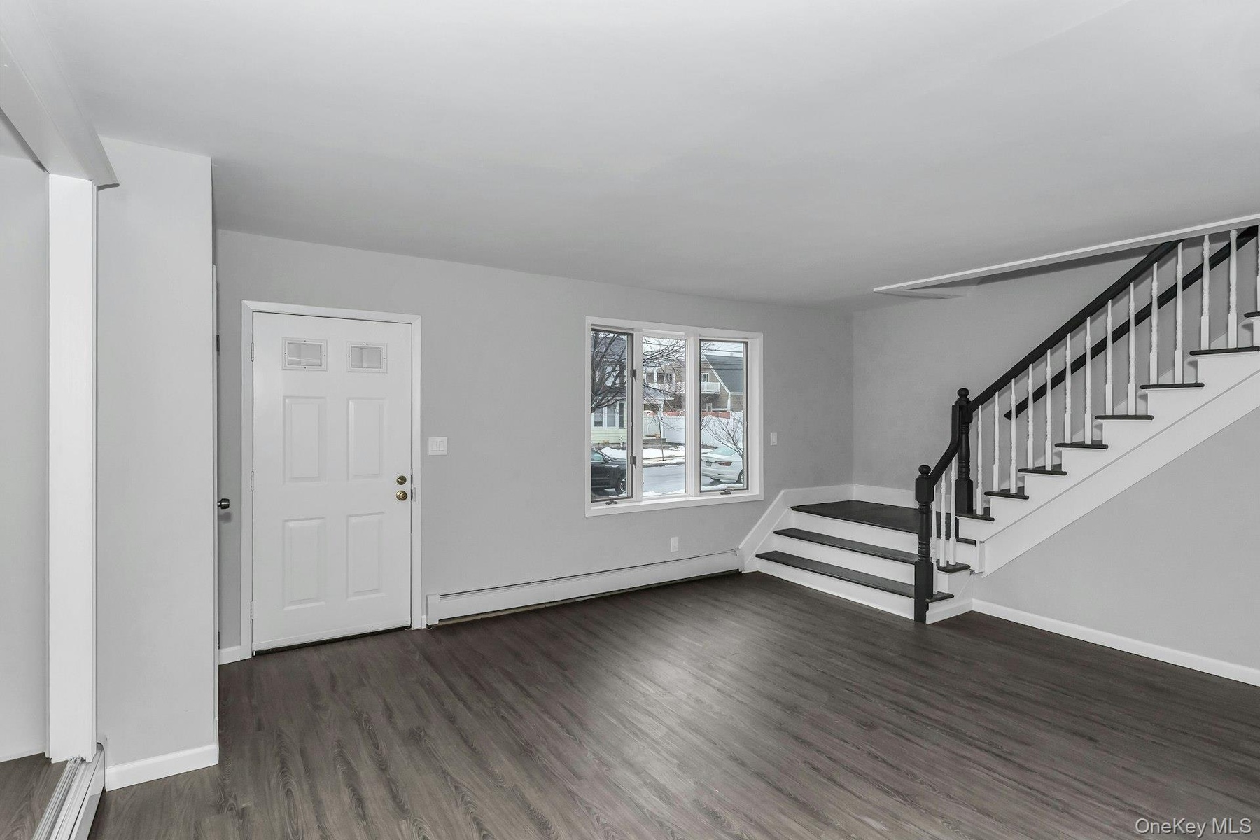 Entryway featuring wood-finish flooring, a contemporary staircase with dark wood-finish handrails and white balusters, and a paneled entry door