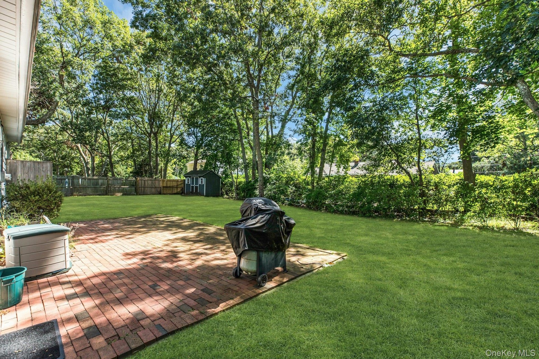 Expansive green lawn with mature trees and a brick paver patio