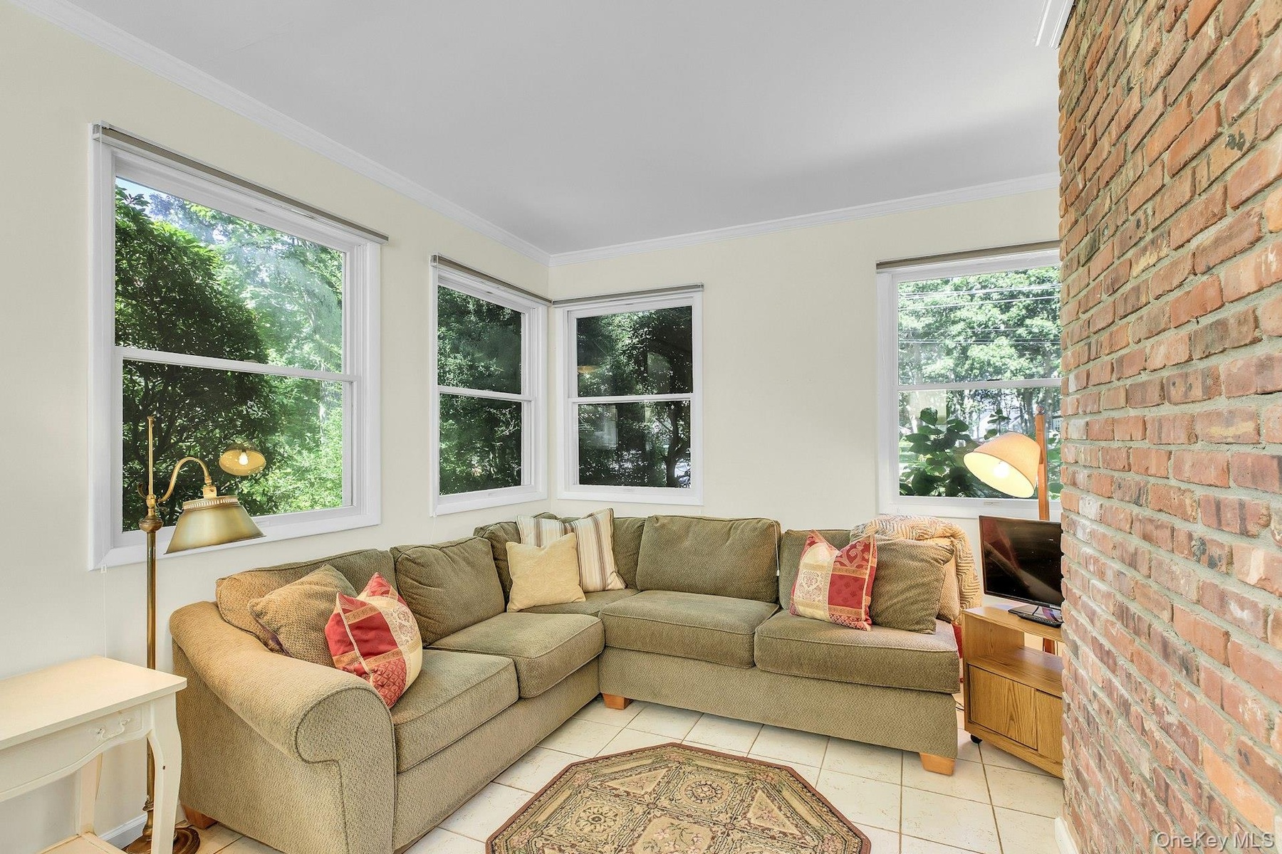 Exposed brick accent wall, multiple windows, crown molding, and tiled flooring