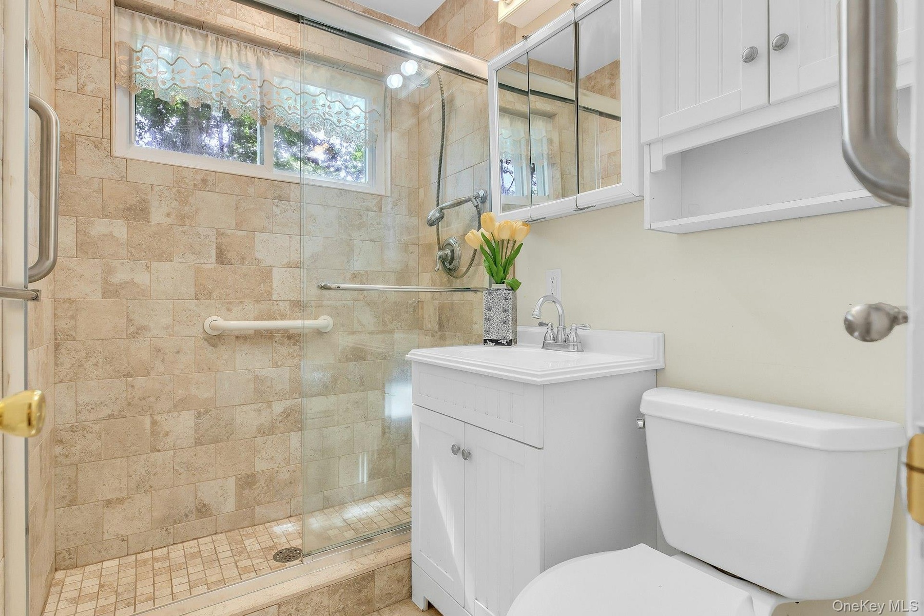 Glass-enclosed shower with full-height tile surround, window, and grab bars