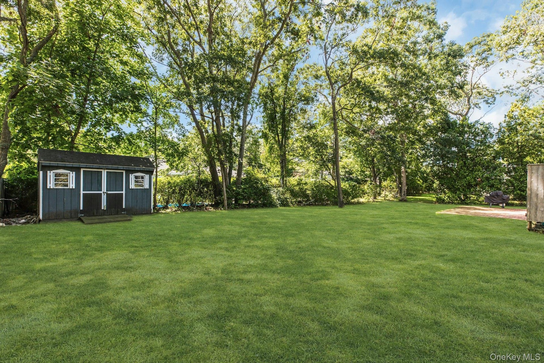 Expansive lawn with mature trees, a detached storage shed featuring double doors, and a gravel area