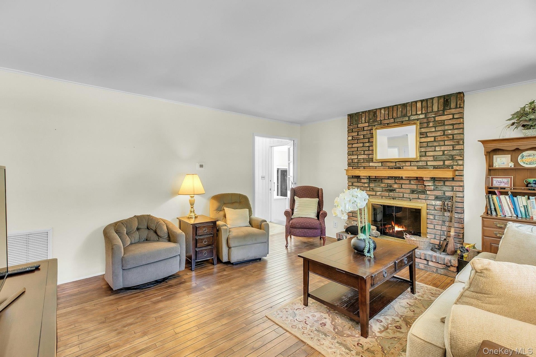 Brick fireplace with a wood mantle, wood-finish flooring, and crown molding