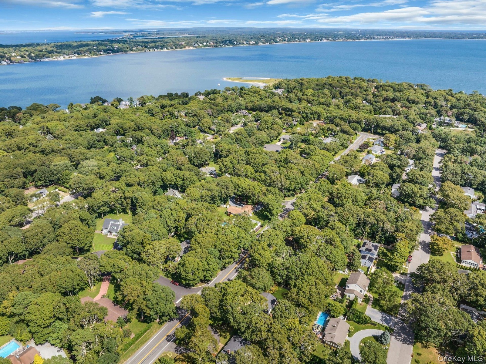 Expansive wooded landscape with winding roads and scattered residential properties, bordered by a large body of water