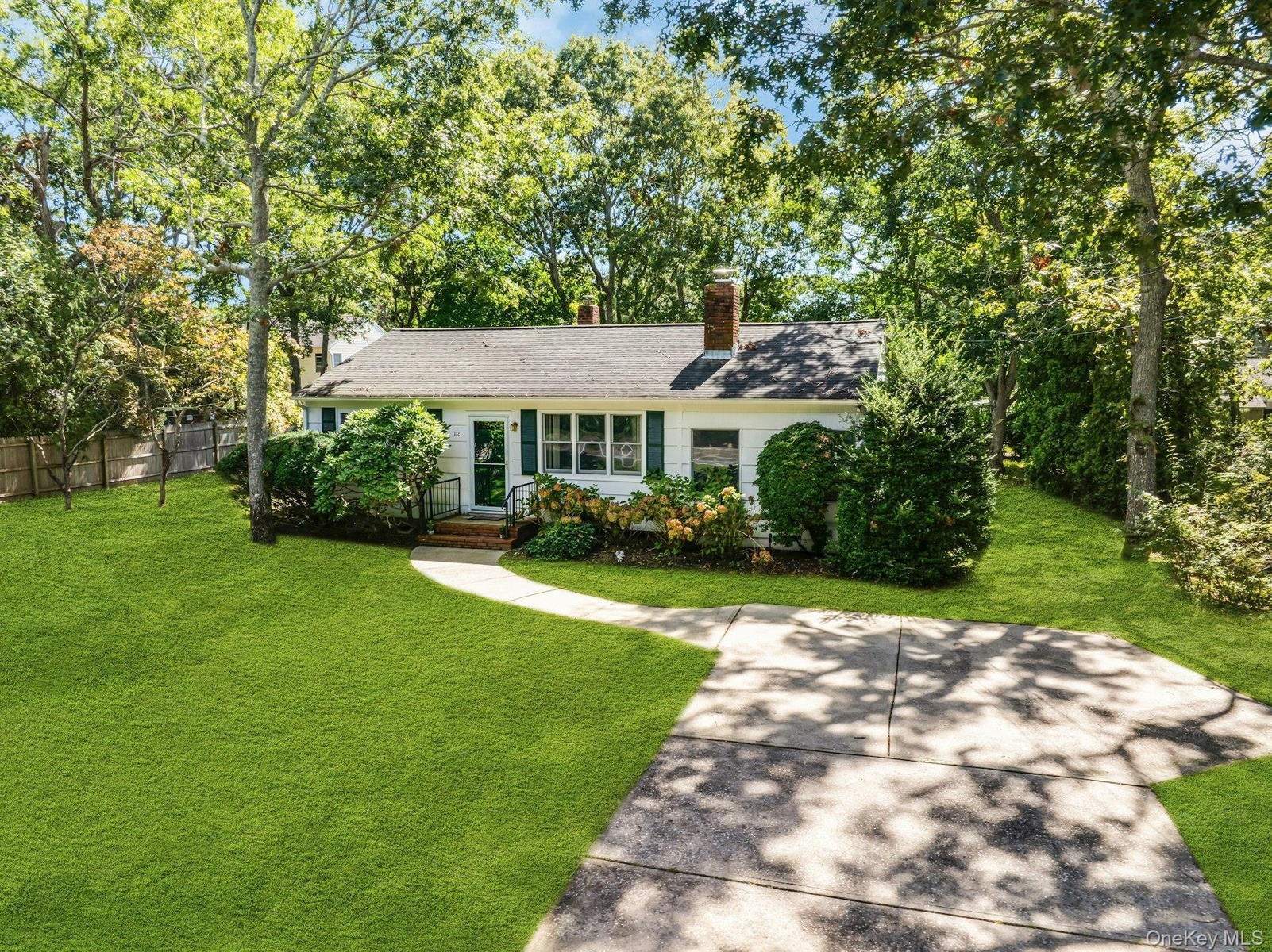 Ranch-style residence featuring white siding, green window shutters, and mature trees