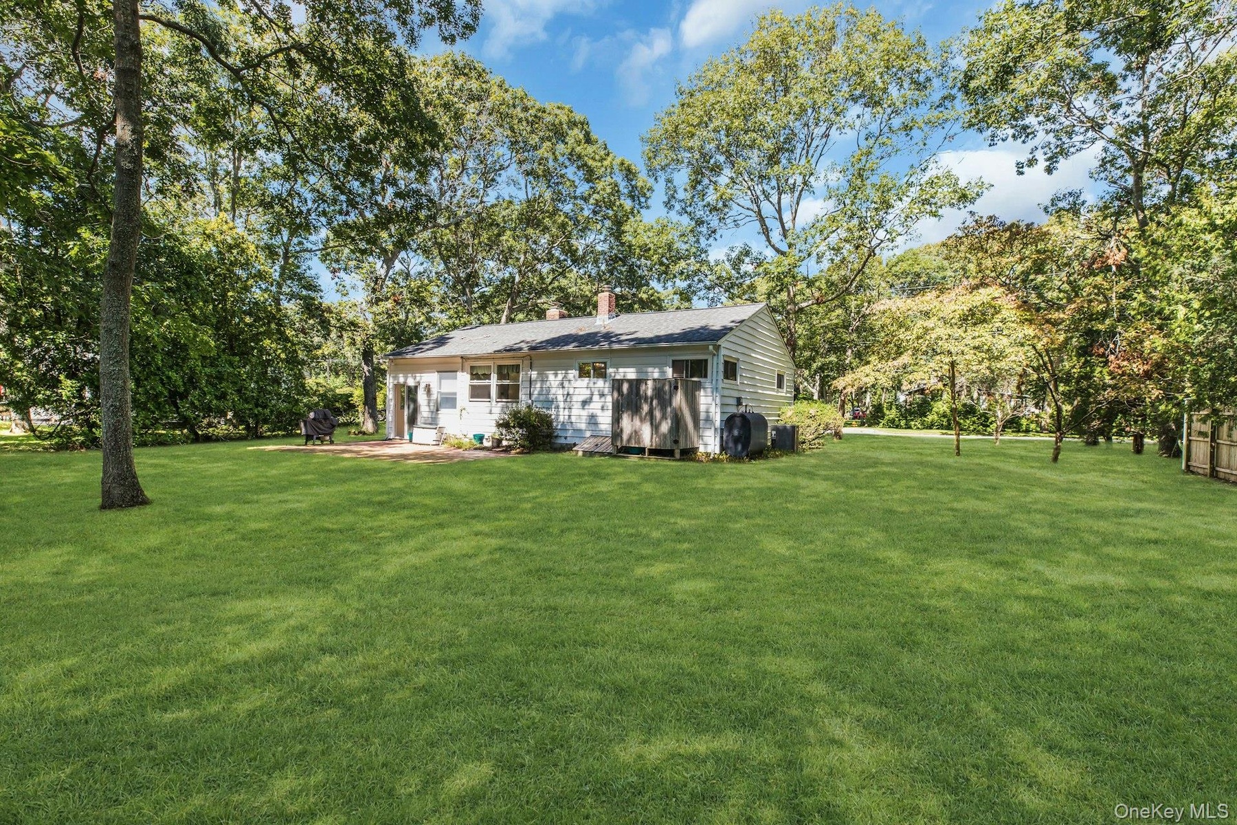 Expansive green lawn, mature trees, white siding exterior, shingle roof, and a paved patio area