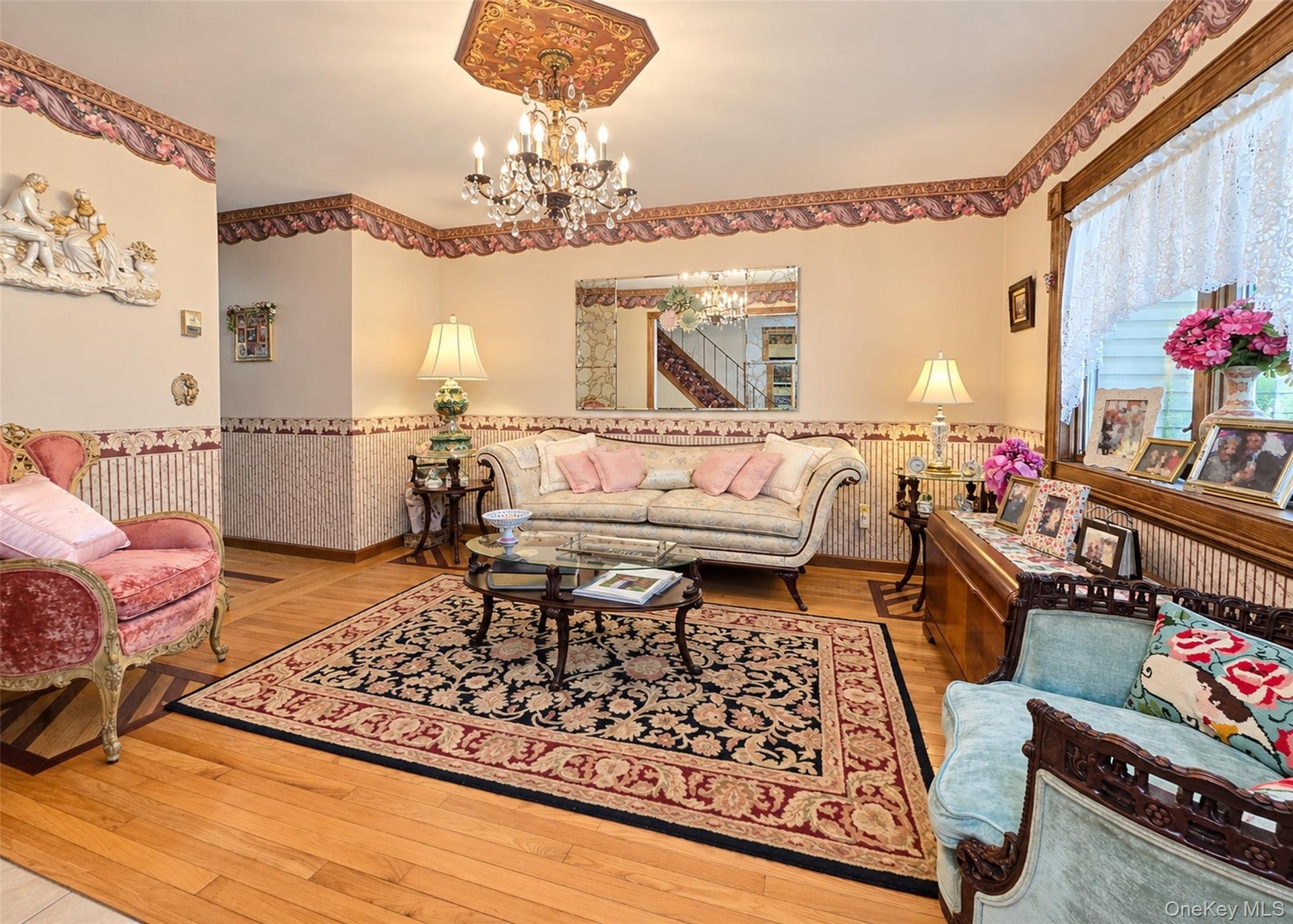 Hardwood flooring with decorative inlay, chandelier with ornate ceiling medallion, decorative wall coverings, window with lace curtain, and built-in w