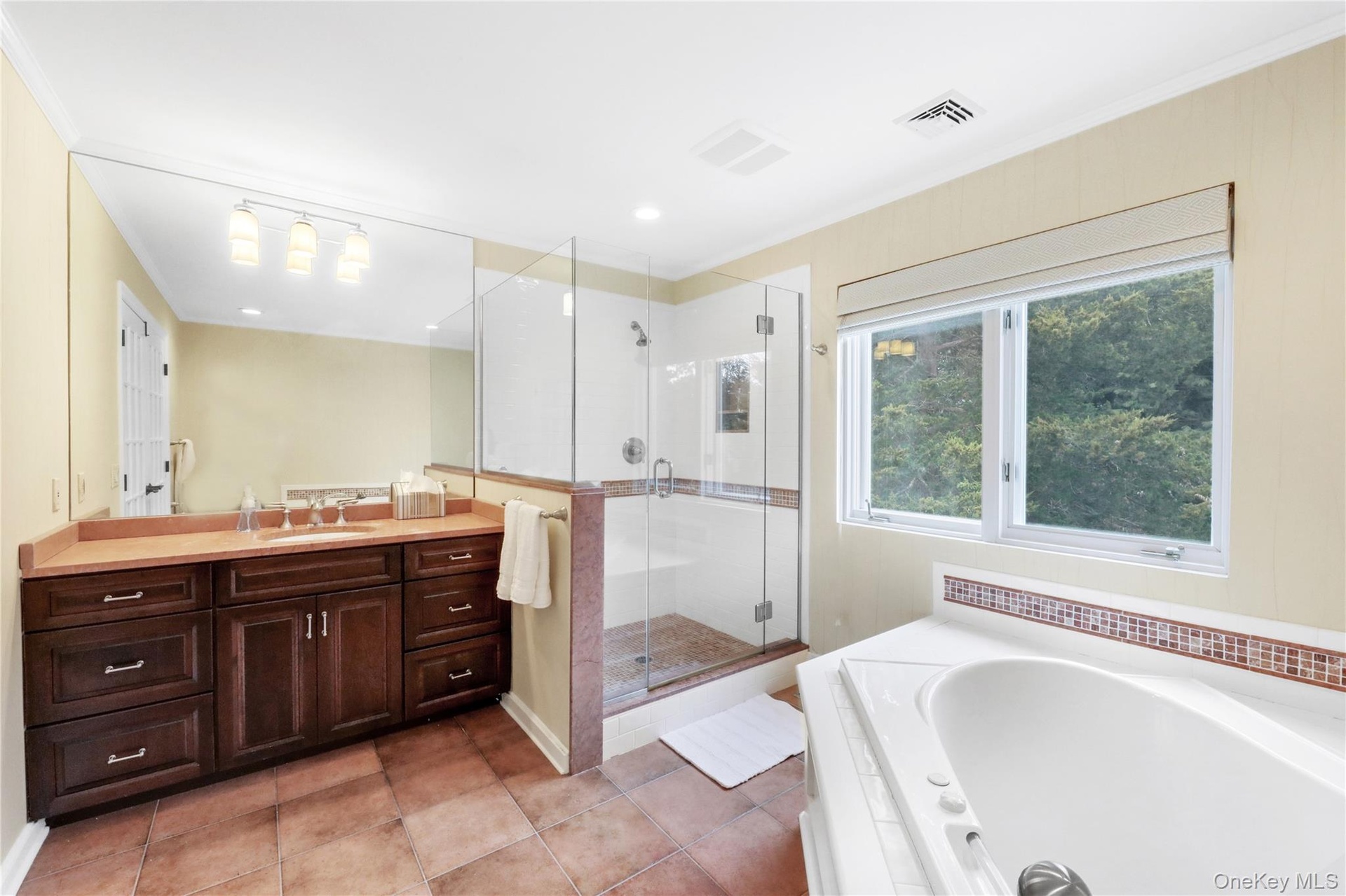 Full bath featuring vanity, a garden tub, a stall shower, light tile patterned flooring, and crown molding